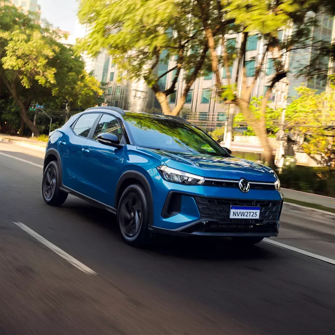 SUV azul dirigindo em uma estrada com fundo desfocado de árvores e prédios.