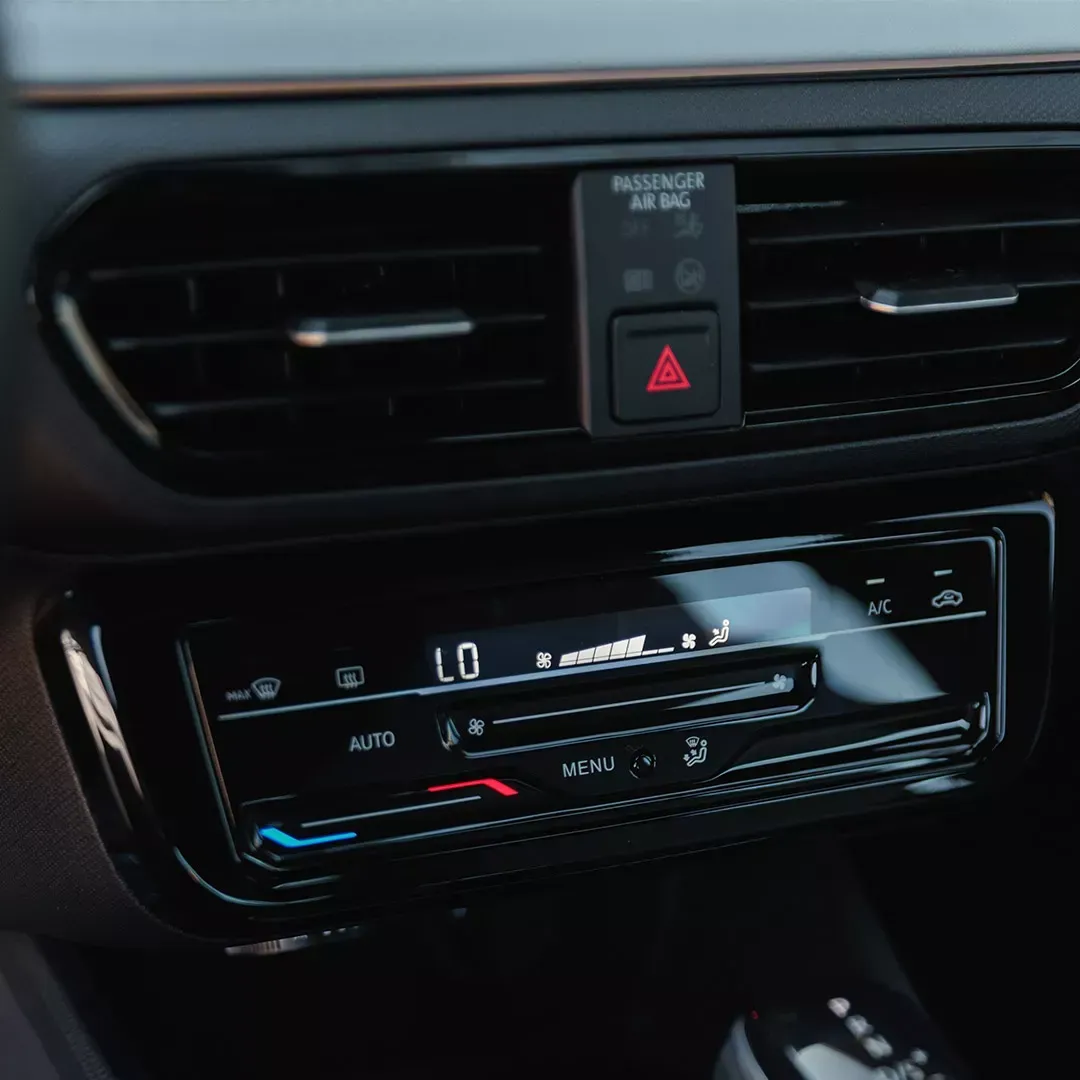 Interior do carro com saídas de ar no painel, controles climáticos e luz de advertência do airbag do passageiro.