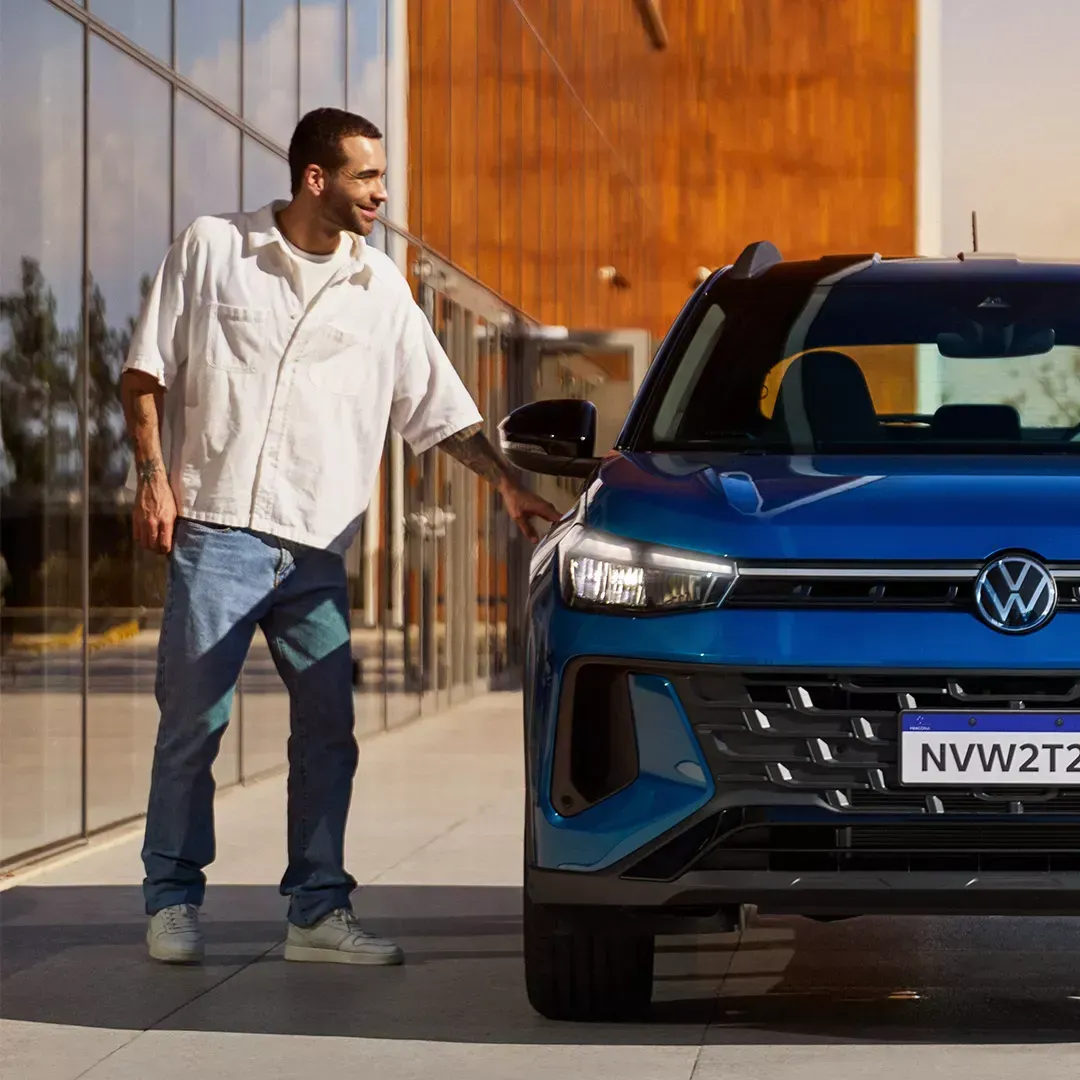 Homem ao lado de um SUV Volkswagen azul, estendendo a mão para alcançar a maçaneta da porta ao ar livre em um dia ensolarado.