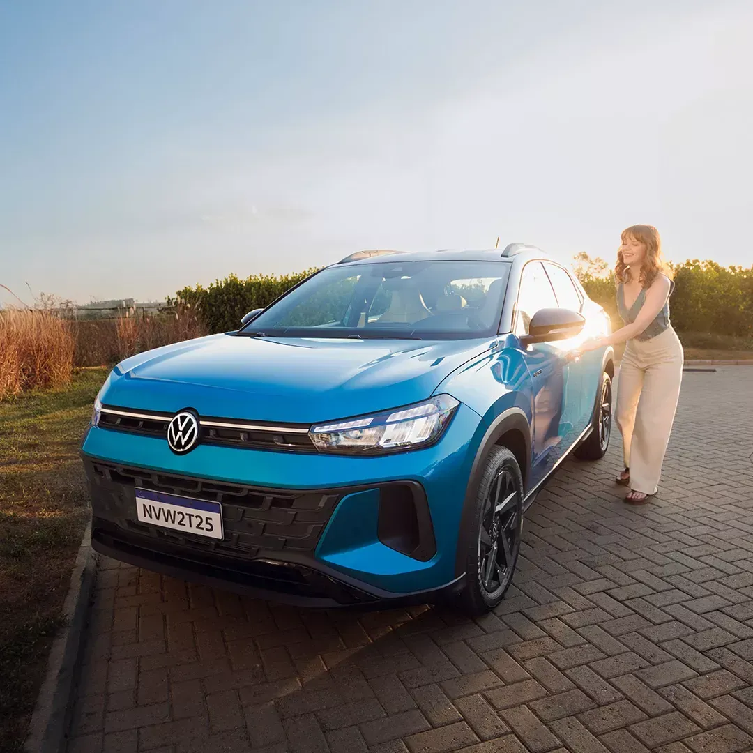 SUV Volkswagen azul estacionado ao lado de uma pessoa em uma estrada de tijolos sob a luz do sol.