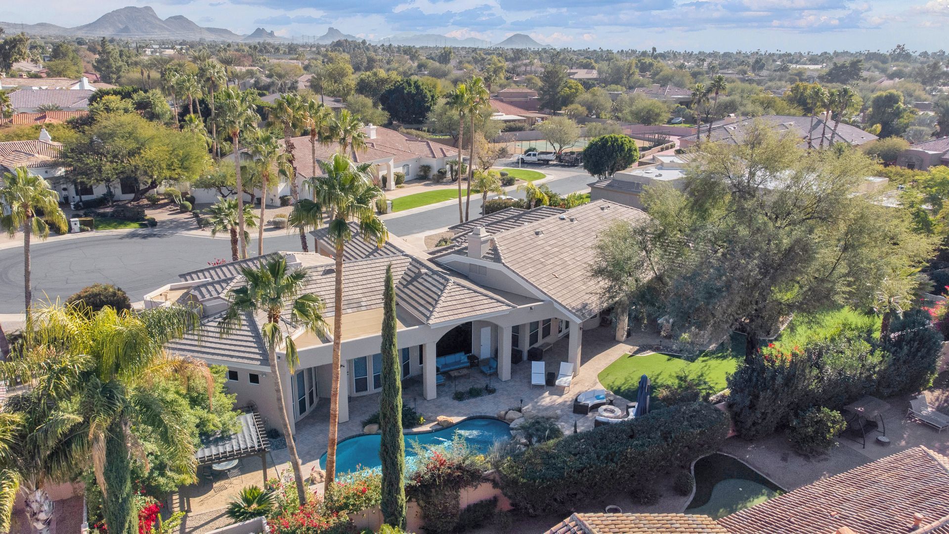 An aerial view of a house with a pool and palm trees in a residential area.