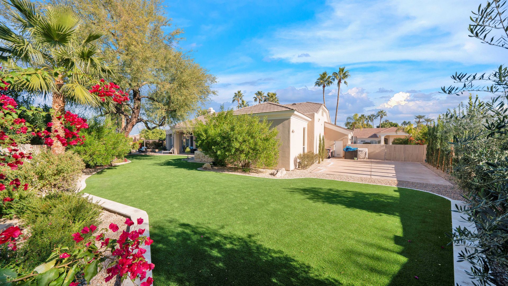 A large lush green lawn in front of a house with palm trees.