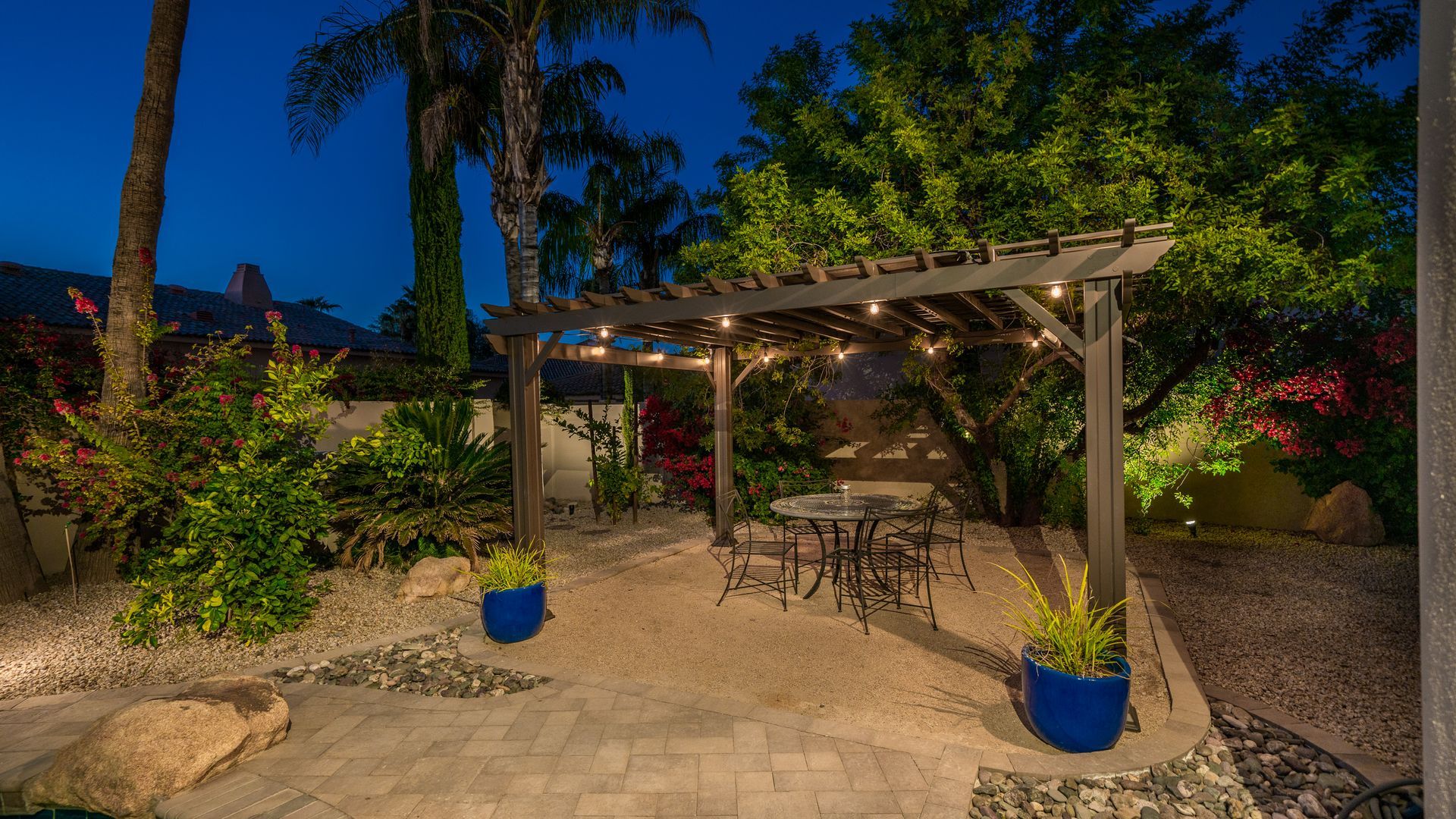 A patio with a pergola and a table and chairs at night.