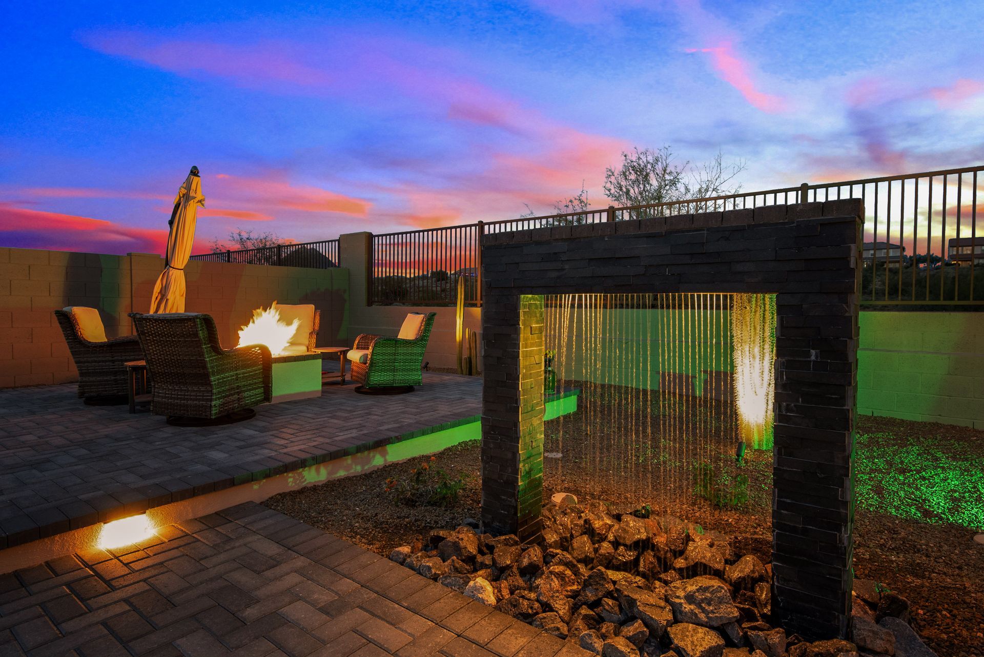 A patio with a fire pit and a waterfall at sunset.
