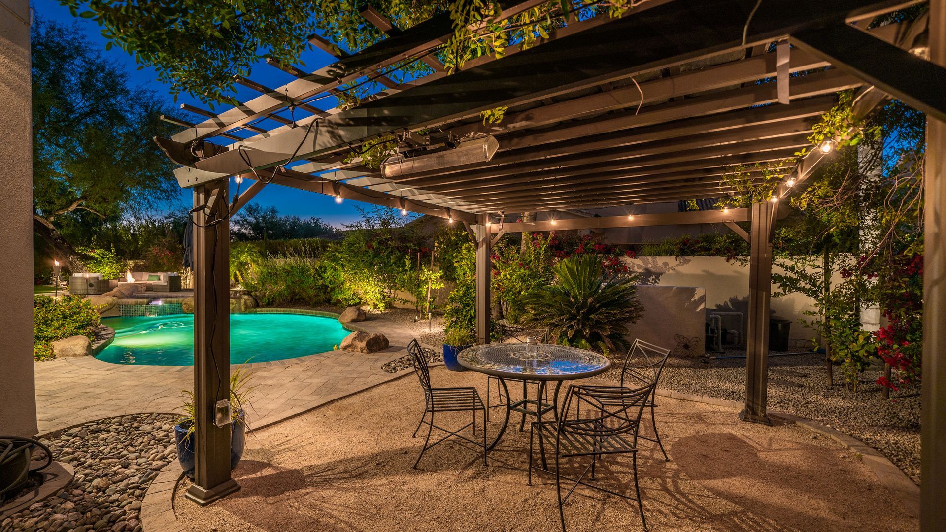 There is a table and chairs under a pergola next to a pool.