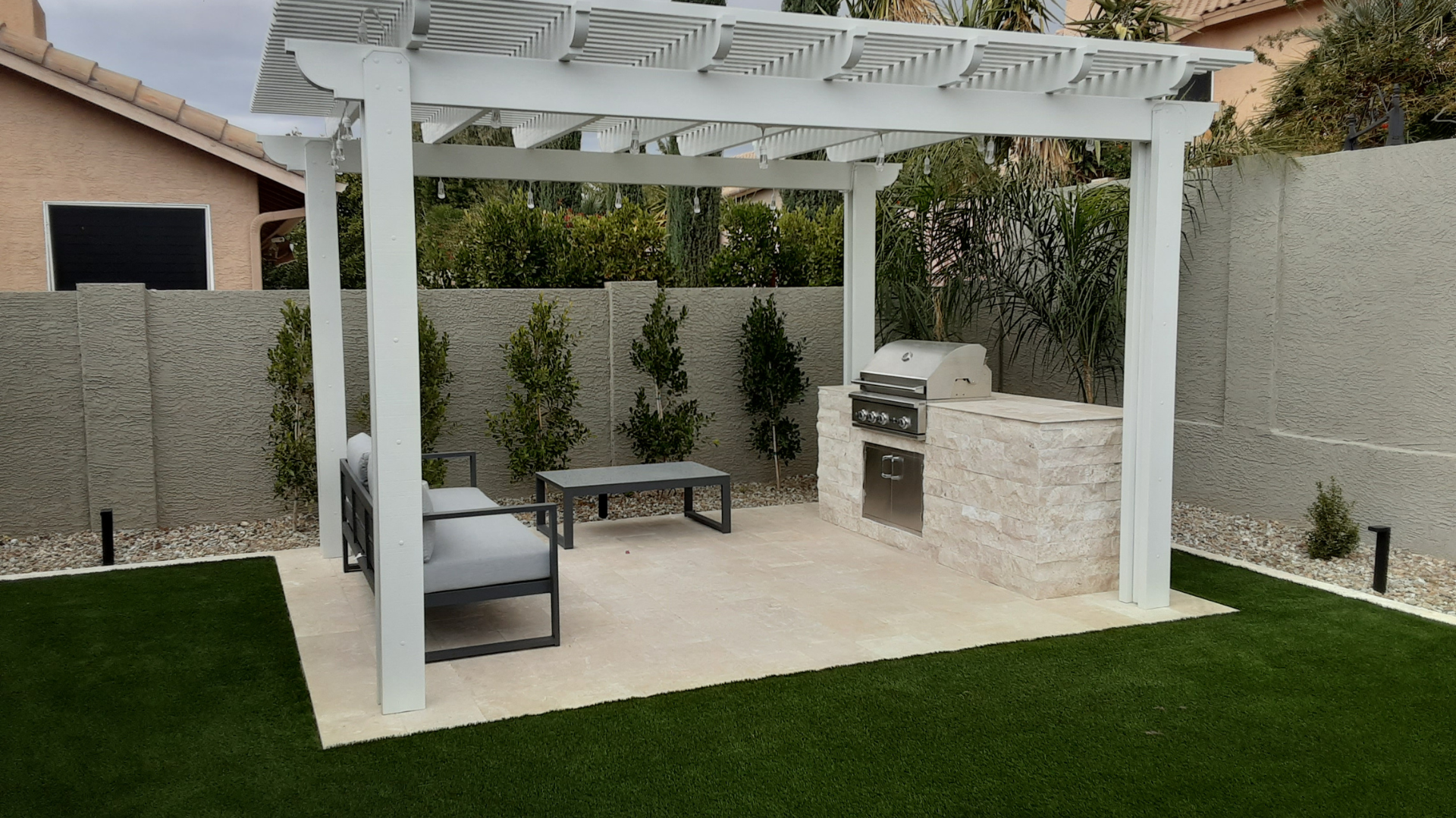 A backyard with a white pergola and a grill.