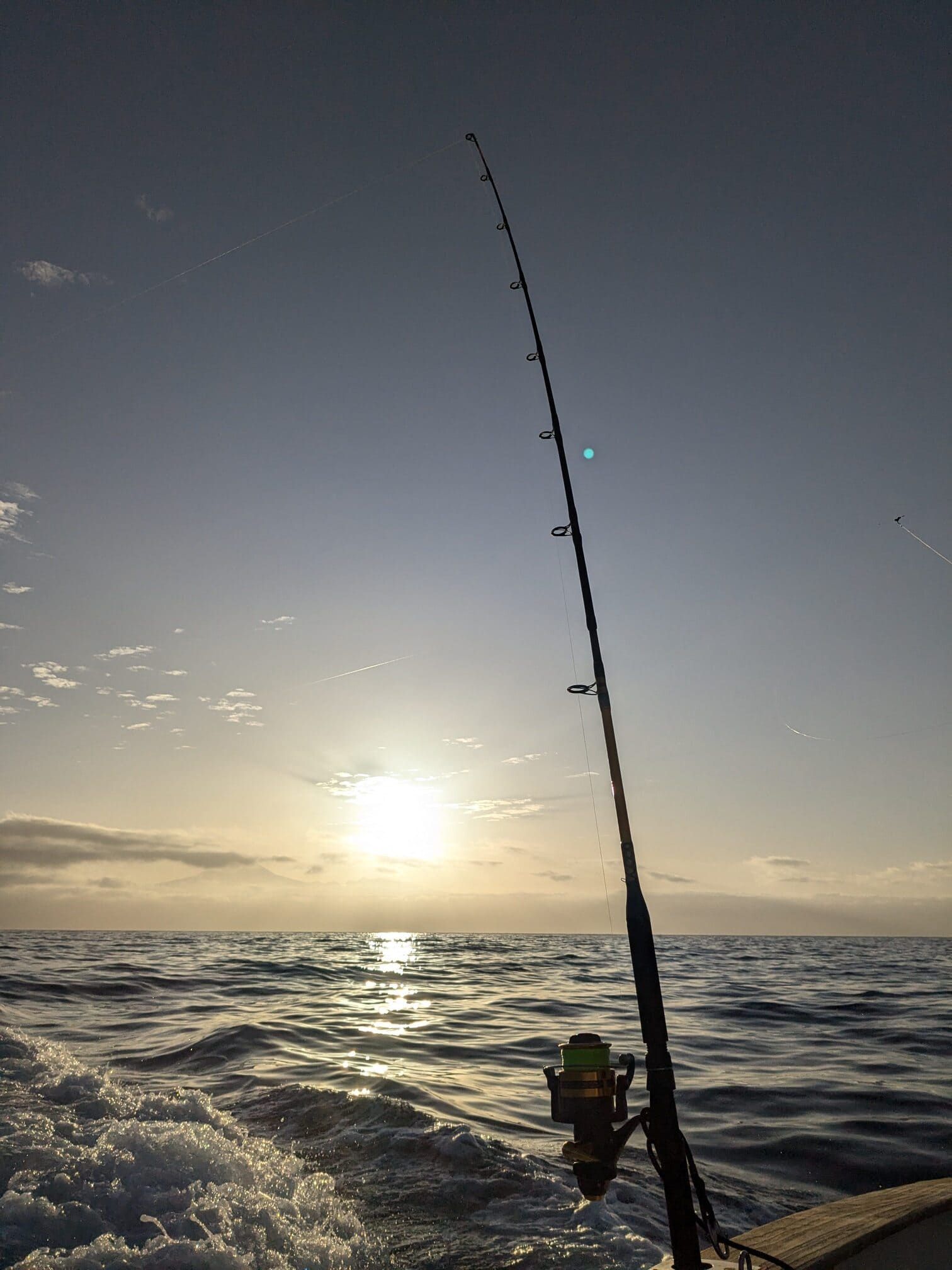 A fishing rod is sitting on a boat in the ocean at sunset.