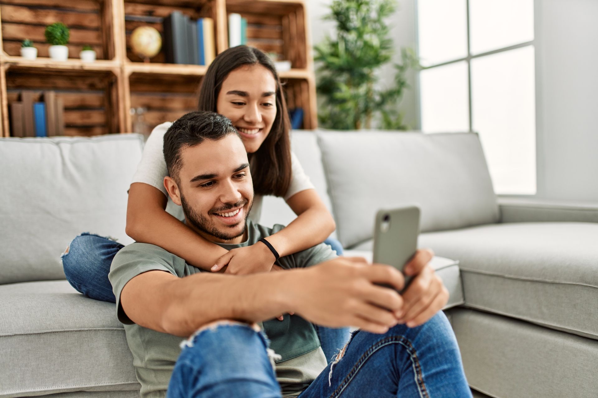 Couple taking a selfie on the floor in front of a couch, smiling.