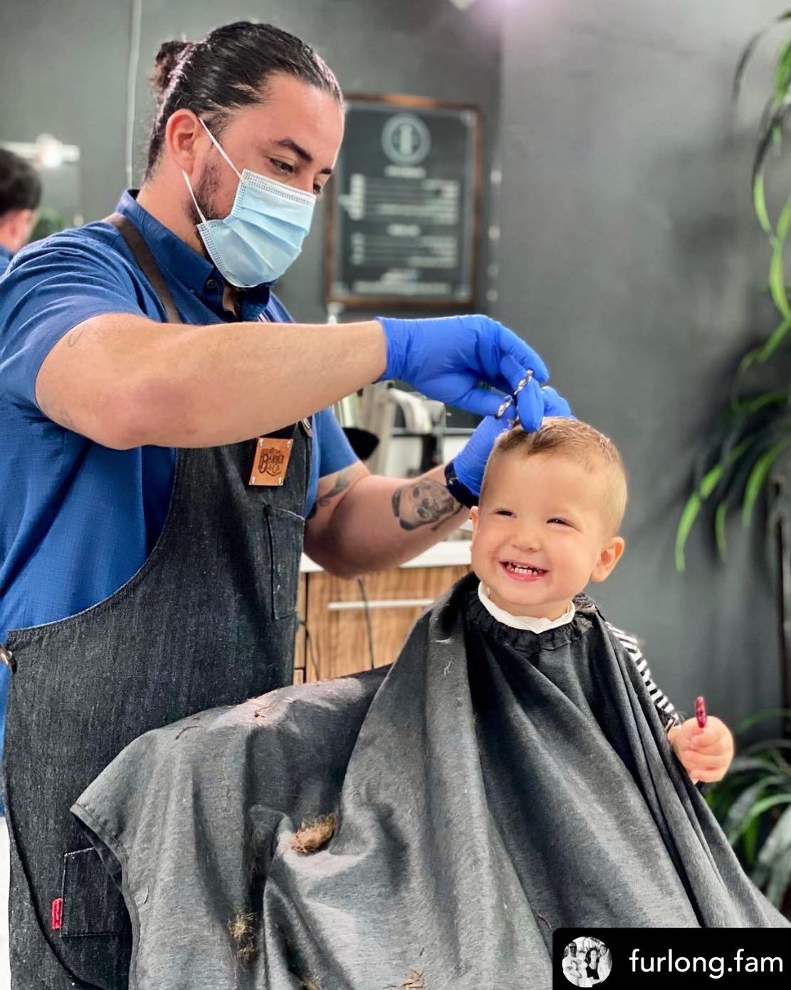 Hairdresser in blue gloves giving a haircut to a smiling child in a salon chair