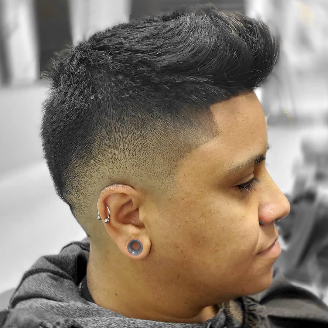 Profile view of a person with a high fade haircut and stretched earlobe piercing in a barbershop chair