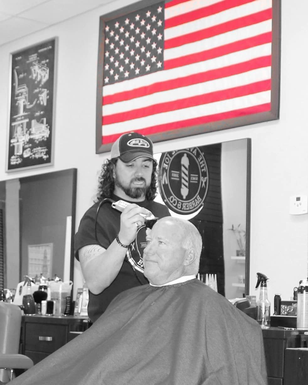 Barber trimming a customer’s beard in a shop with an American flag on the wall.