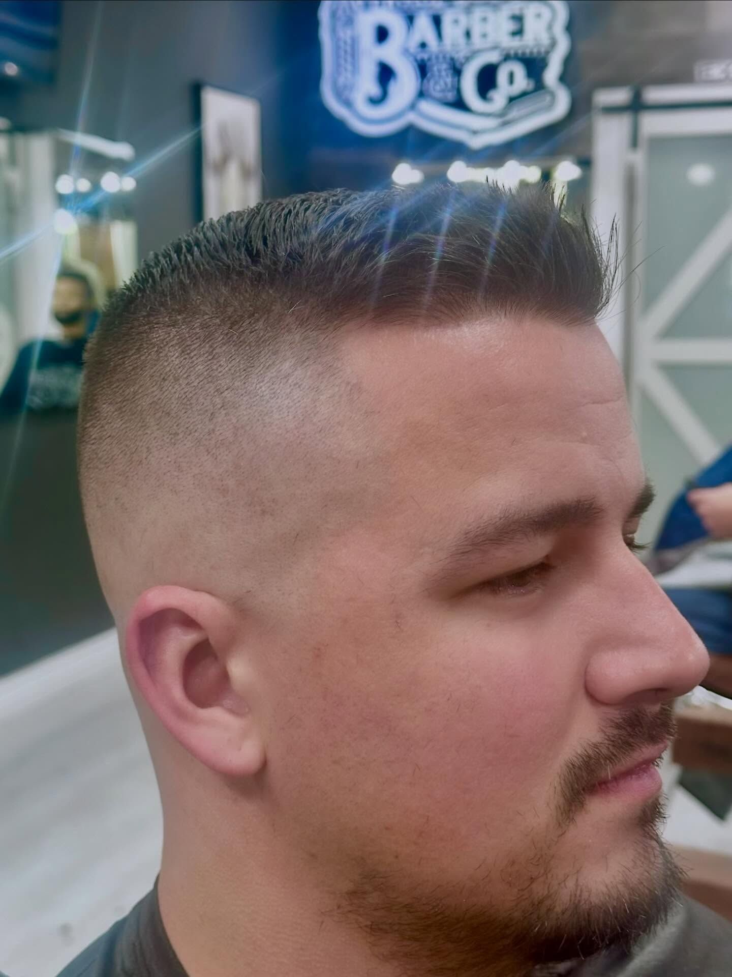 Close-up profile of a man with a short fade haircut and trimmed beard in a barbershop