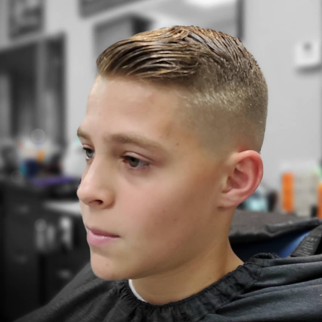 Close-up of a young person with a short fade haircut in a barbershop, wearing a black cape, looking left.