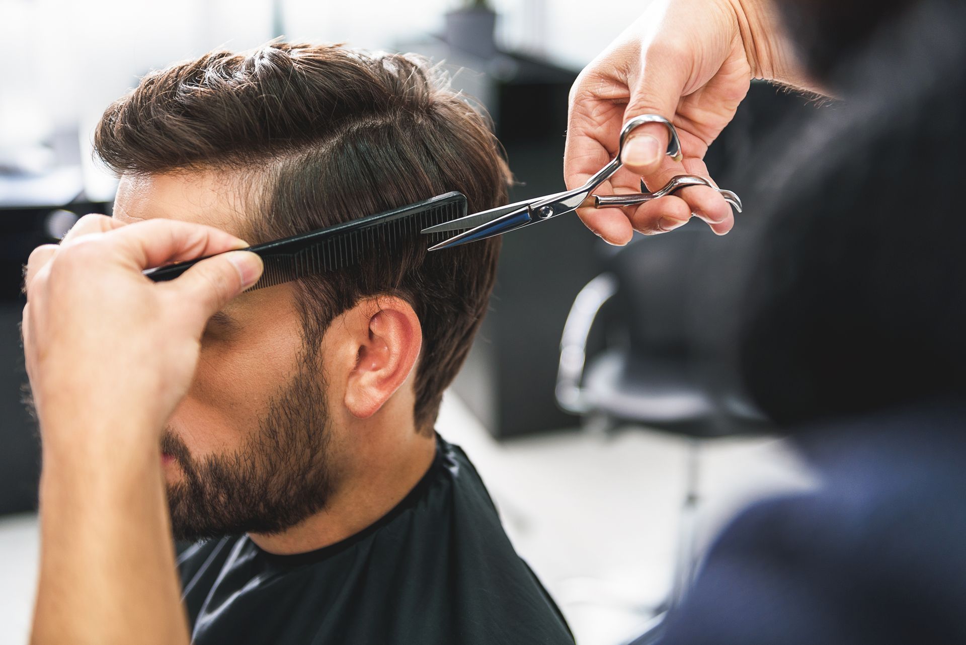 Barber trimming a man’s hair with scissors in a salon