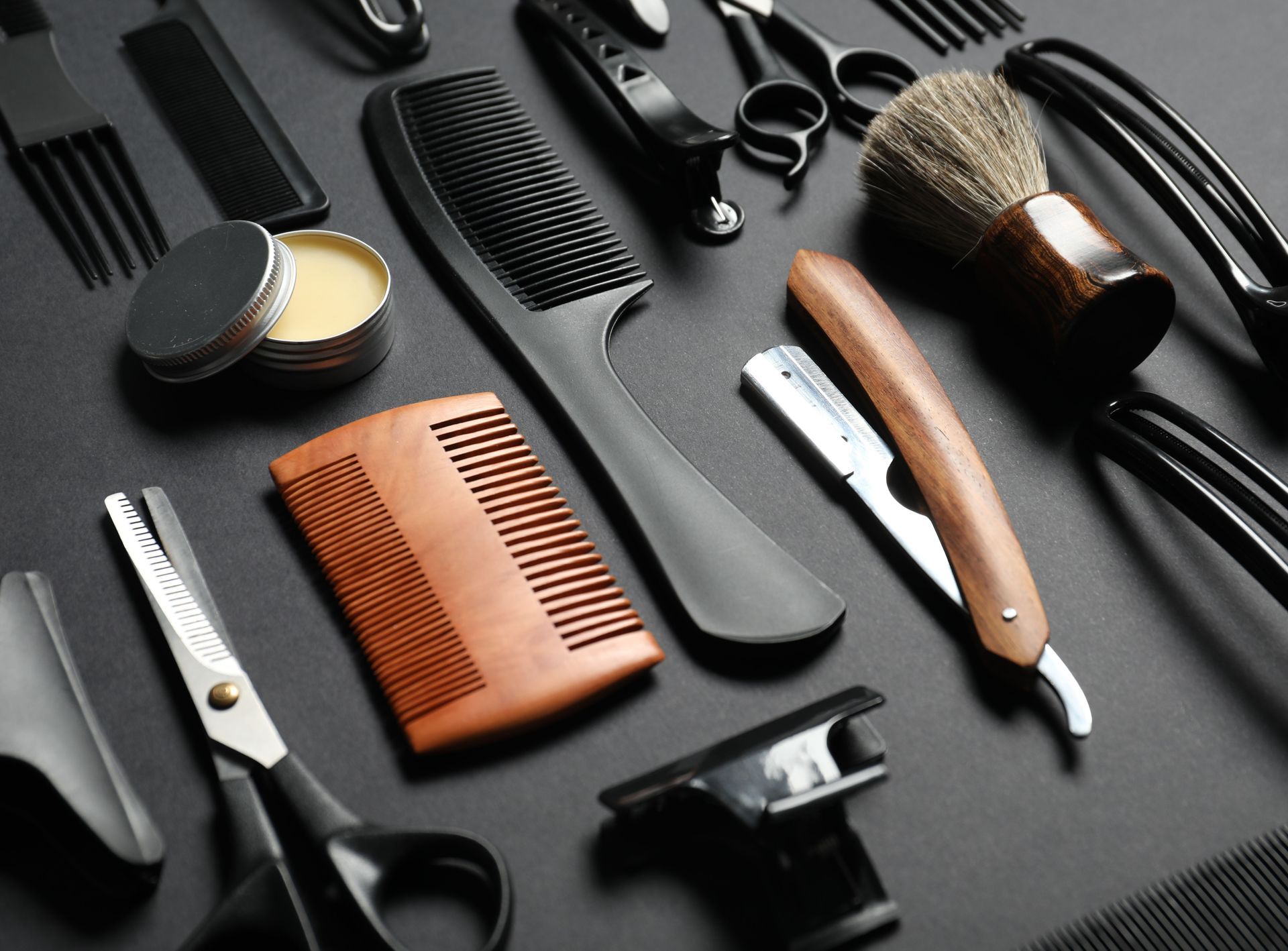 Assorted black and wooden grooming tools and brushes arranged on a dark surface.