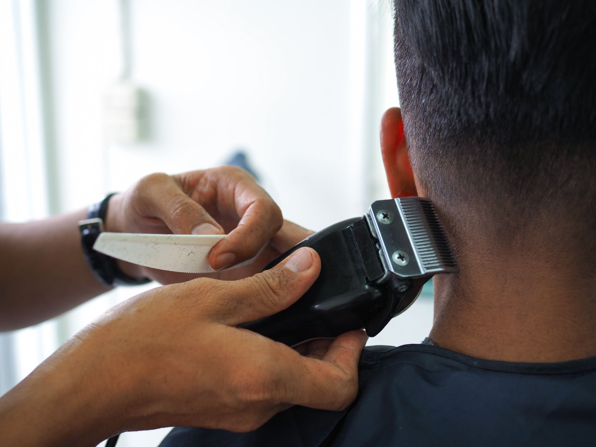 Person trimming another person’s hair with electric clippers at a close-up barbering session