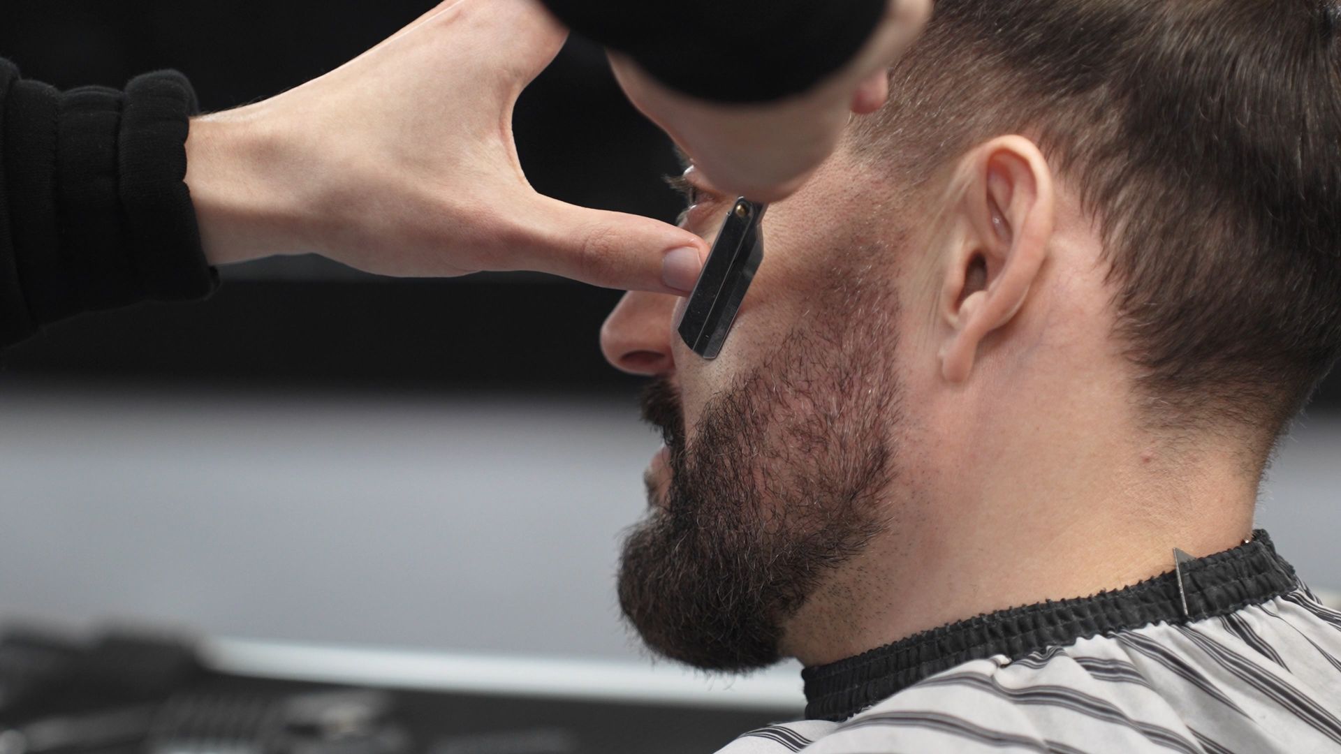 Barber trimming a man's beard with clippers in a barbershop