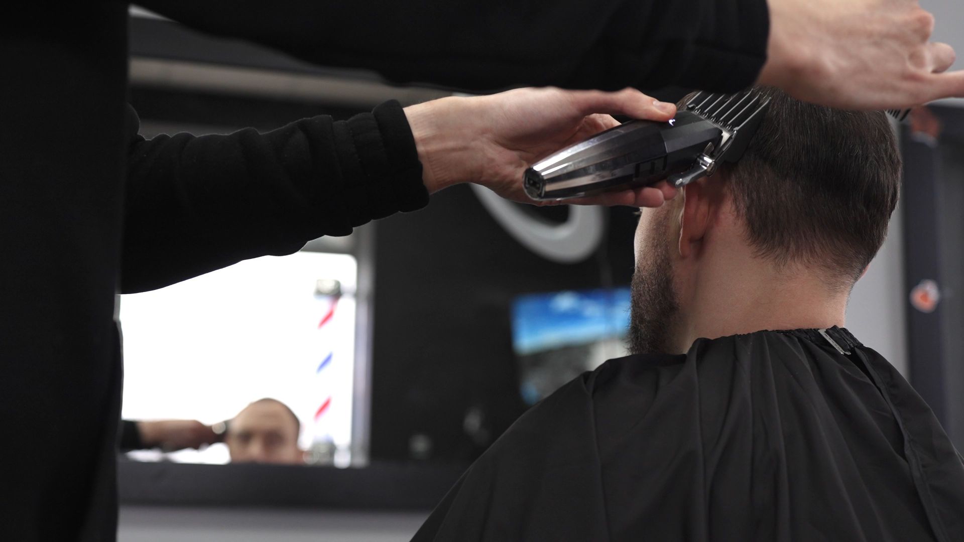 Barber trimming a client’s hair with clippers in a salon, viewed from behind.