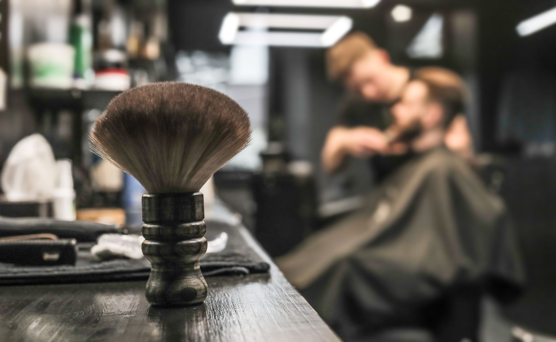 Shaving brush on a barber’s counter, with a blurred customer getting a haircut in the background