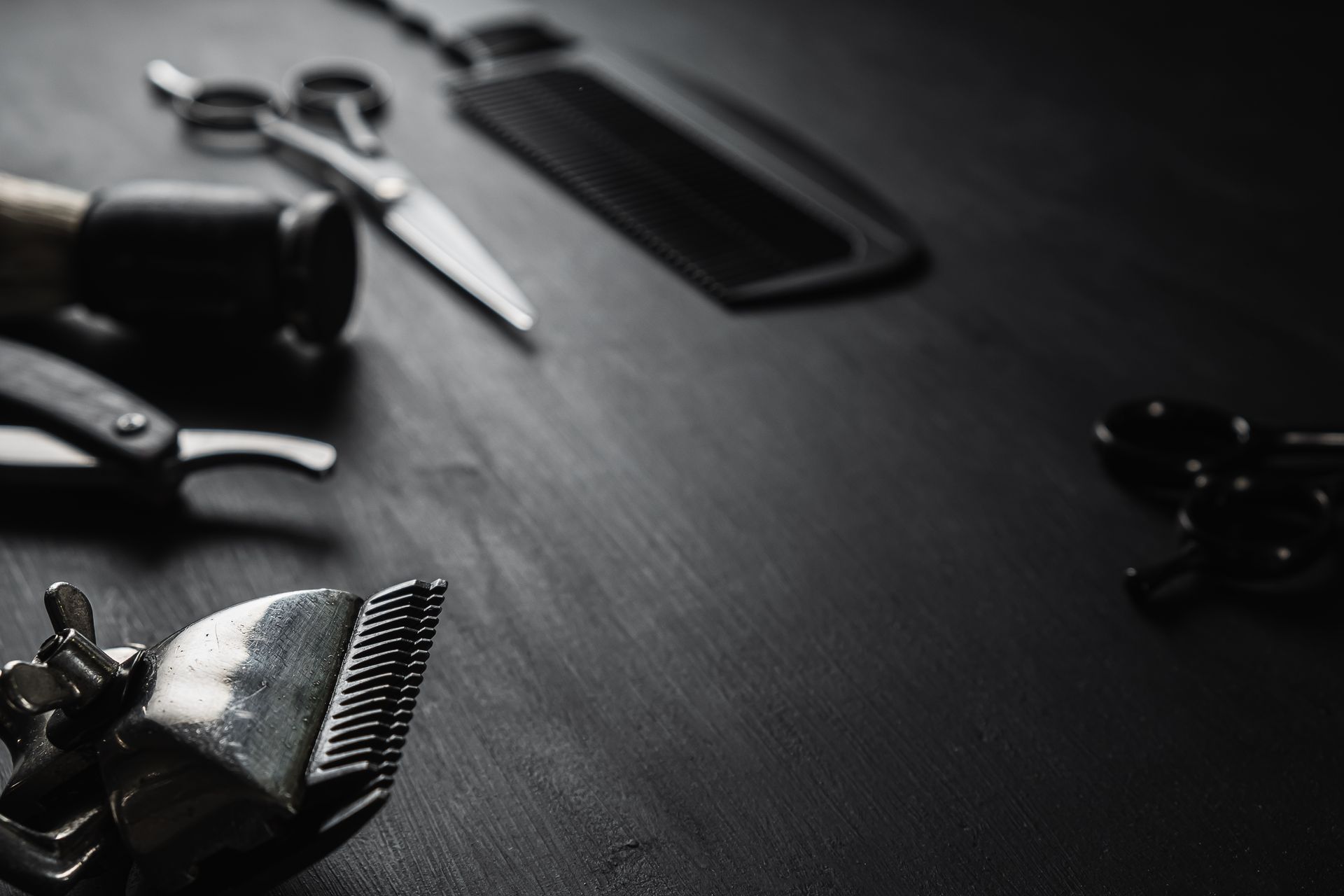 Black-and-white close-up of grooming tools on a dark table, including scissors and hair clippers.