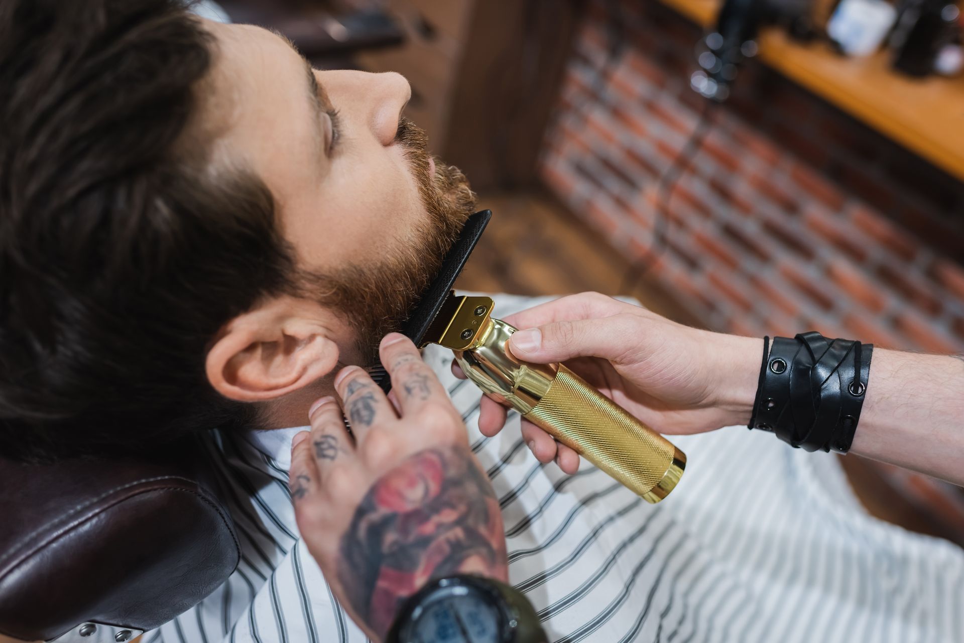 Barber trimming a man’s beard with clippers while he reclines in a salon chair