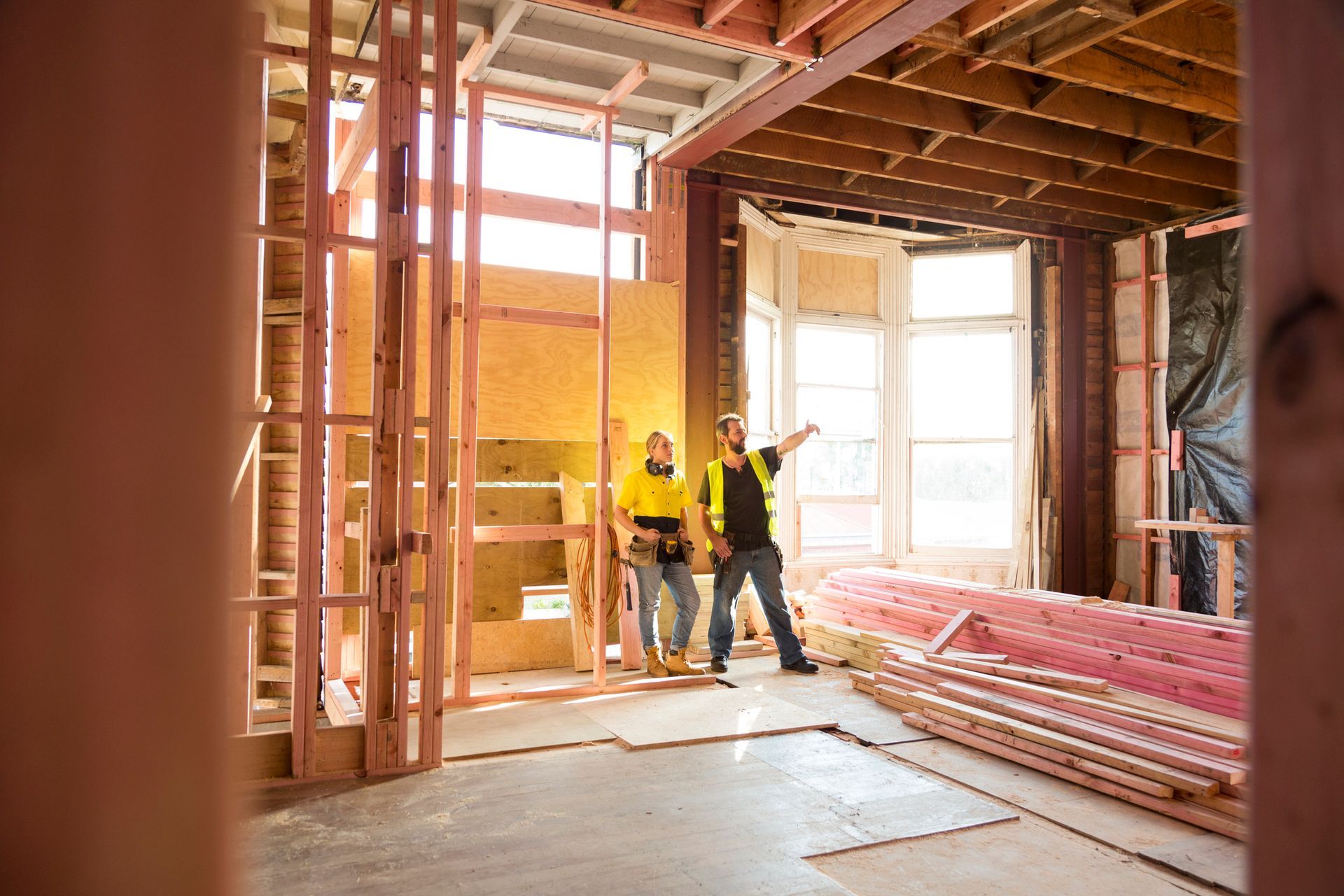 Two construction workers talk together inside large house under renovation.