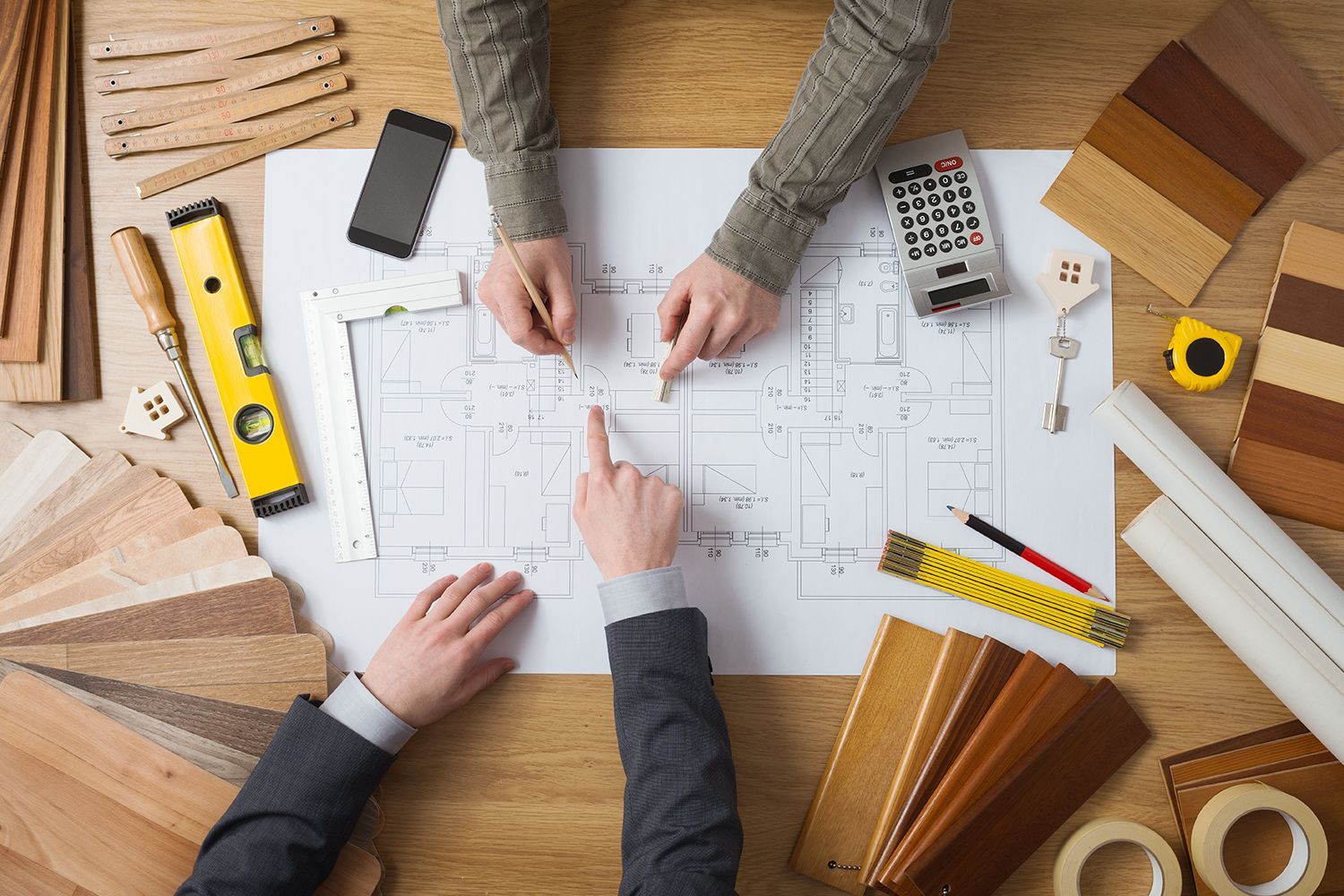 Two people reviewing home floor plans surrounded by wood samples and remodeling tools.