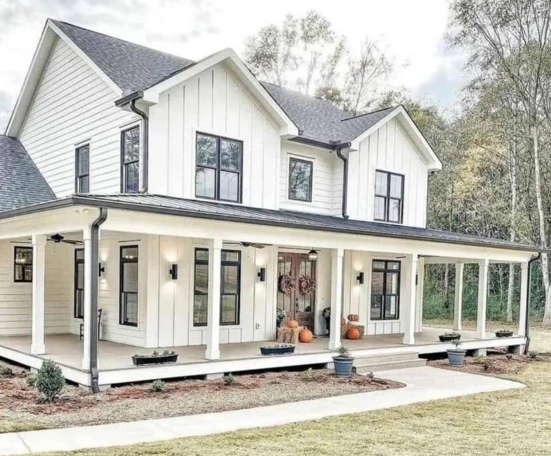 Modern custom-built farmhouse with white siding, black windows, and a spacious wraparound porch.