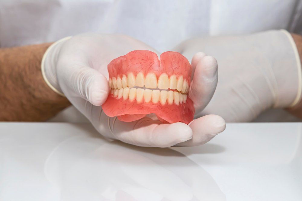 Dentist holding Denture — Dental Services In Sarina, QLD
