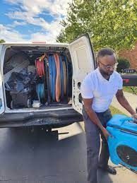 A man is standing in front of a van with a vacuum cleaner in the back.