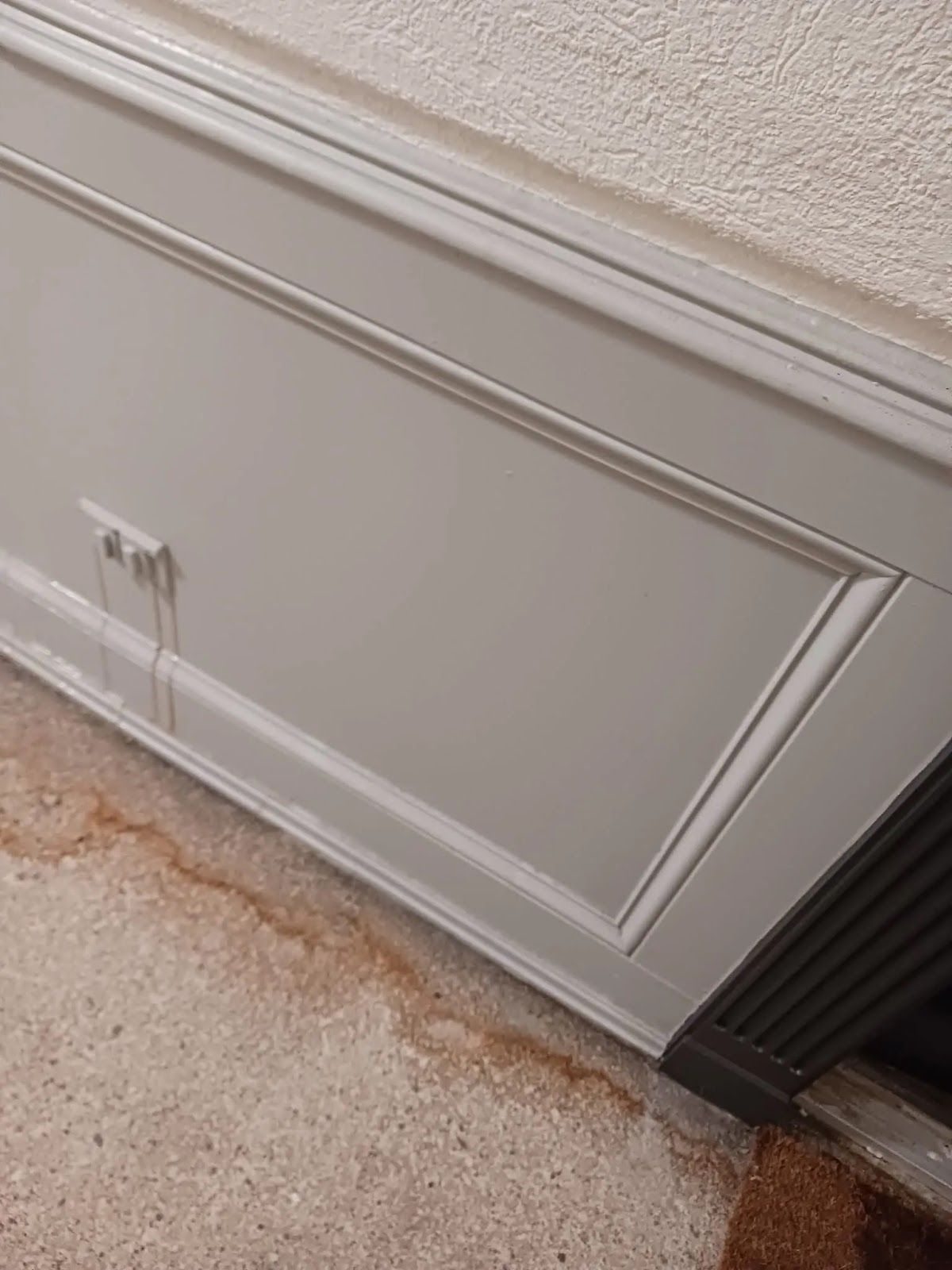 White wall paneling with decorative molding and a dark vent beside a beige carpeted floor.