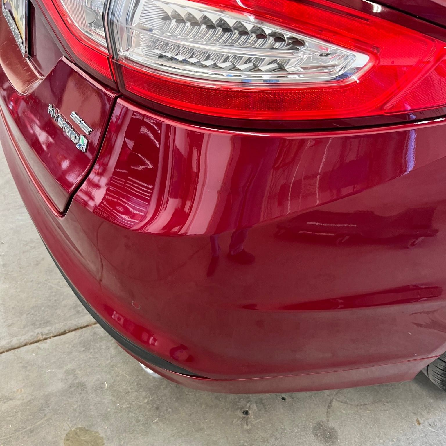 A red car with a damaged bumper is parked in a garage.