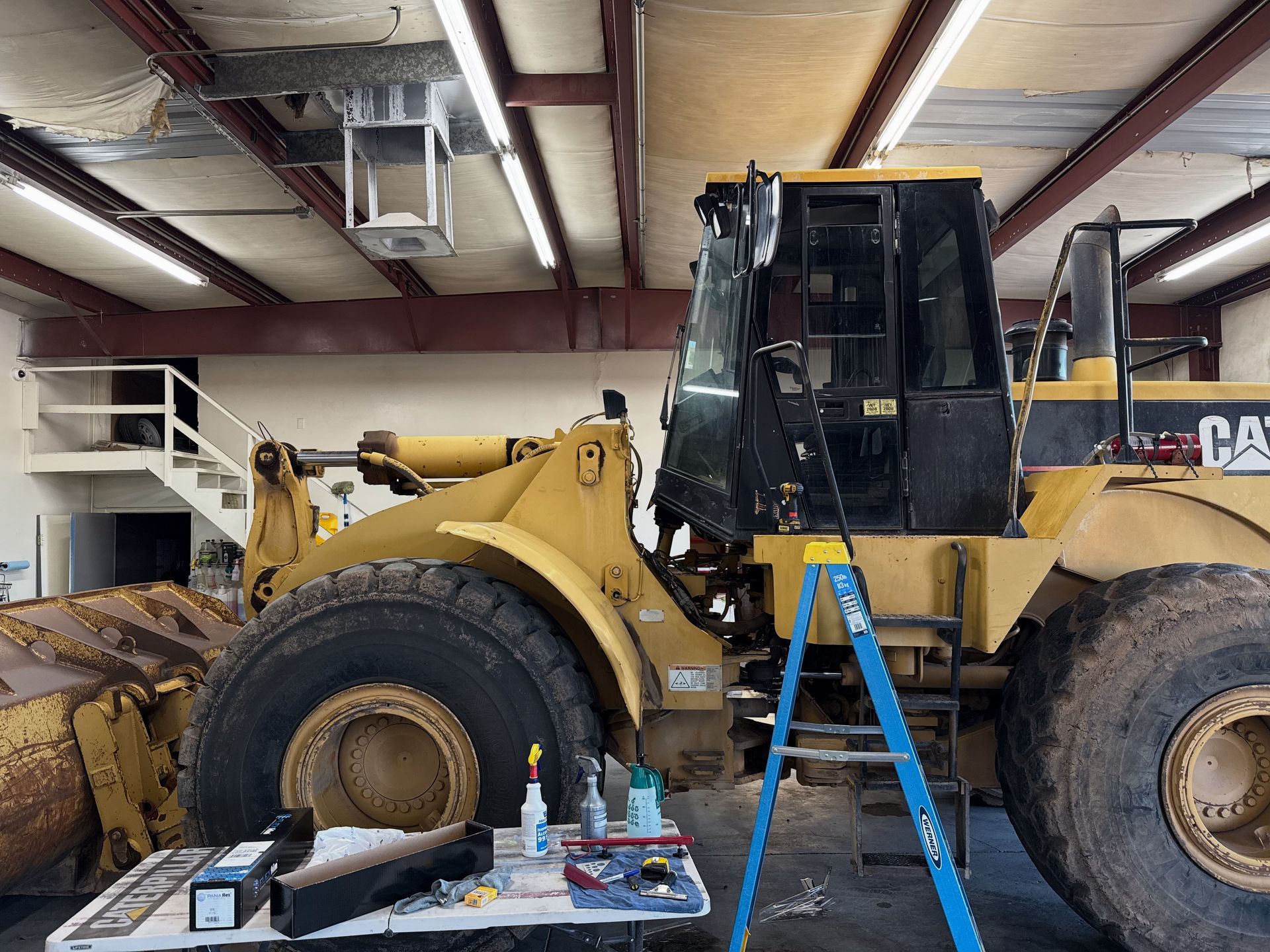 Yellow Caterpillar front loader inside a garage, with blue ladder and tools nearby.