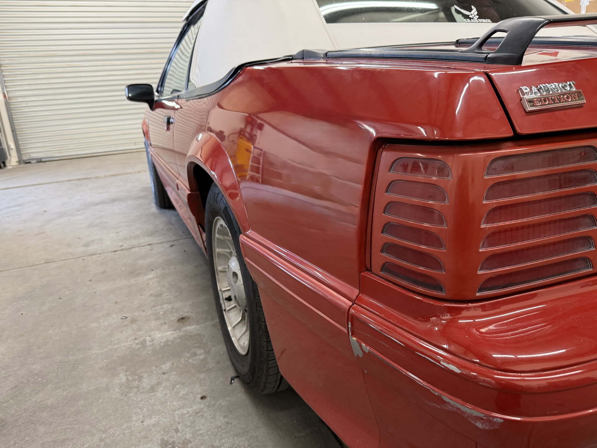 Red convertible Ford Mustang, showing the rear and side, in a garage.