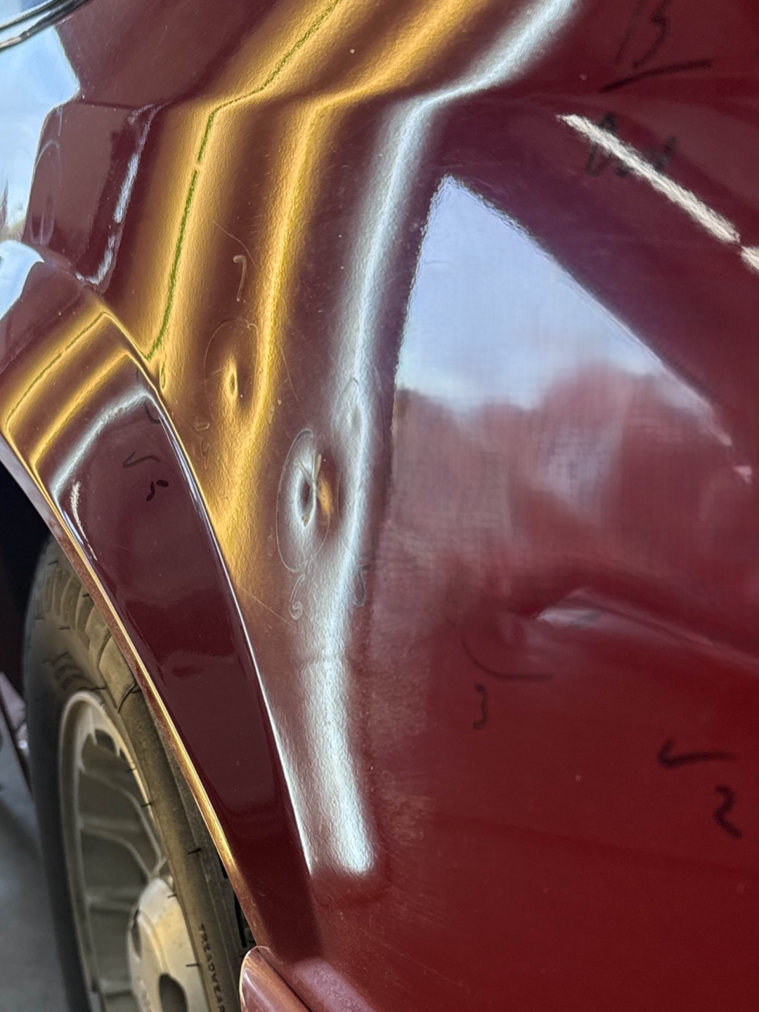 Red car fender with two dents, lit by overhead lights reflecting in the paint.