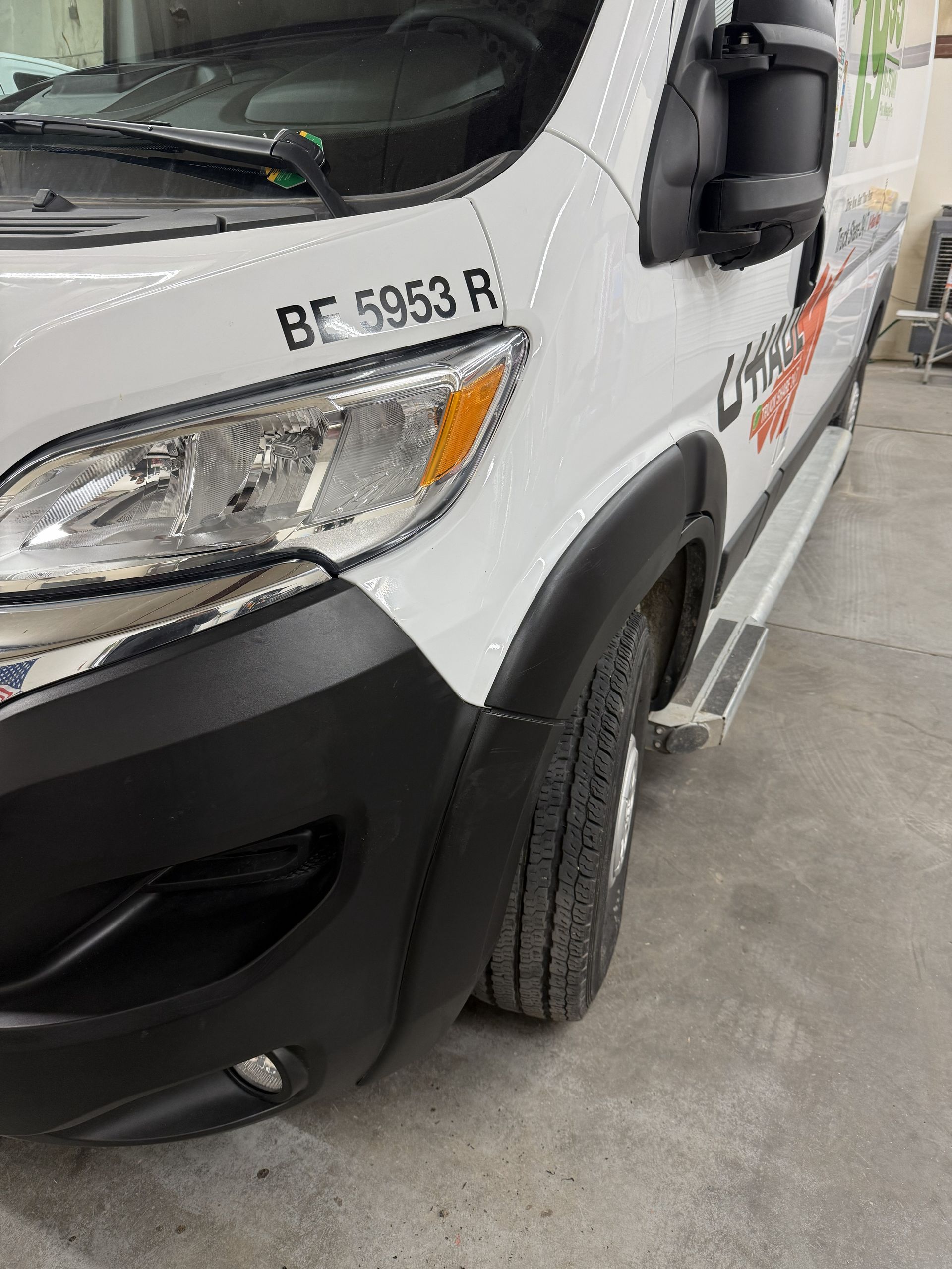 White commercial van, partially visible, parked on a concrete surface, with a black fender and the license plate