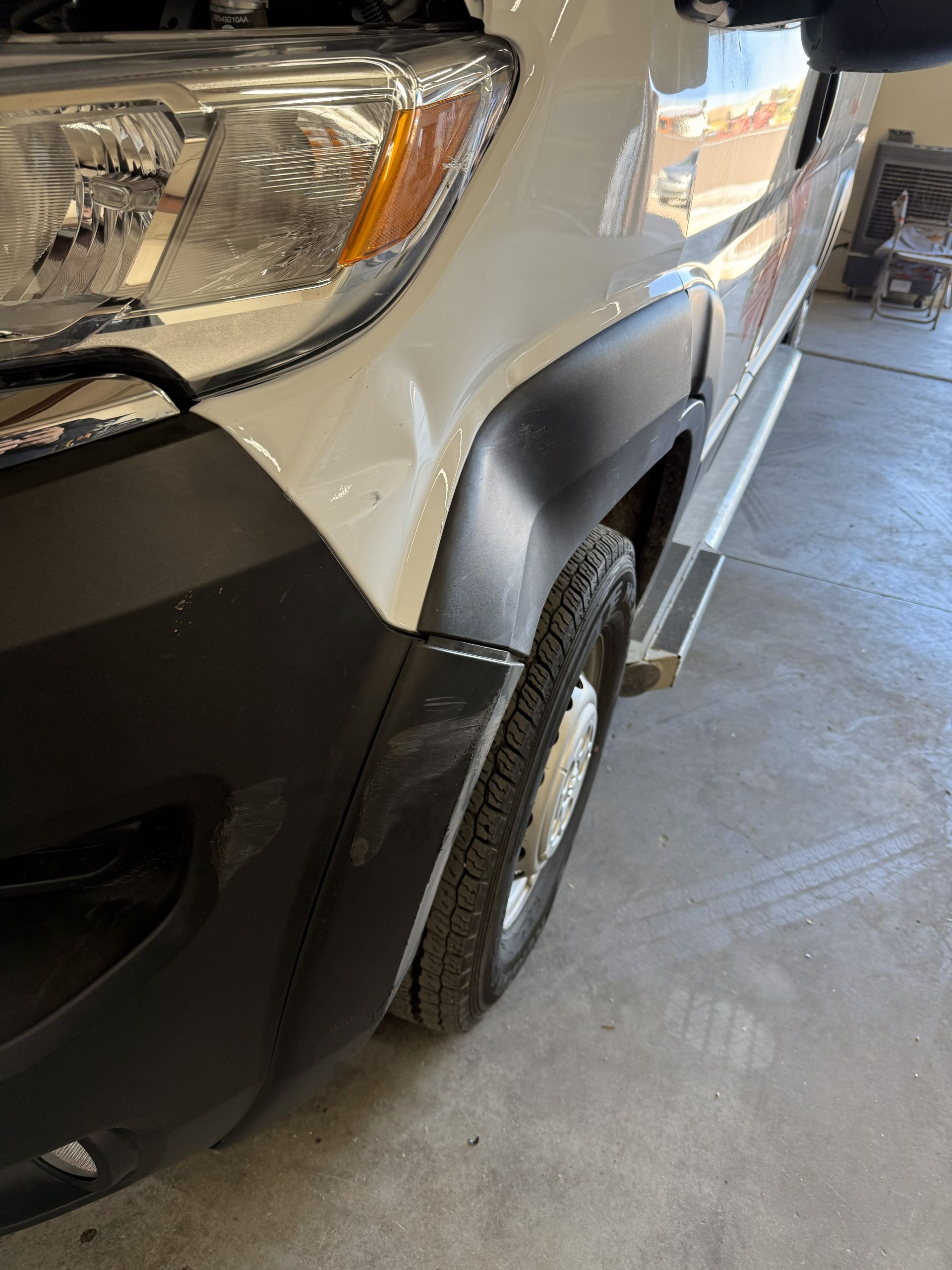 White van, black fender, tire, and headlight. Angle view outdoors, on concrete.