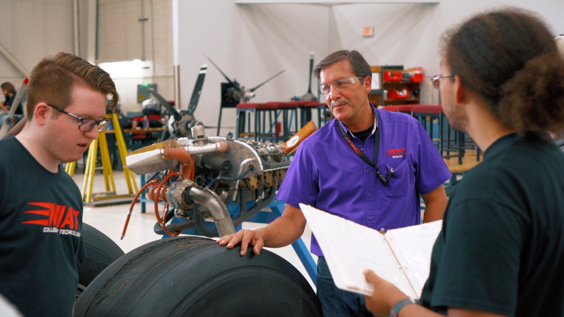 A group of people are standing around a tire in a factory.