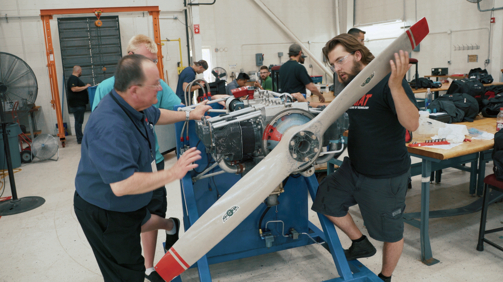 Two men are working on an airplane propeller in a factory.
