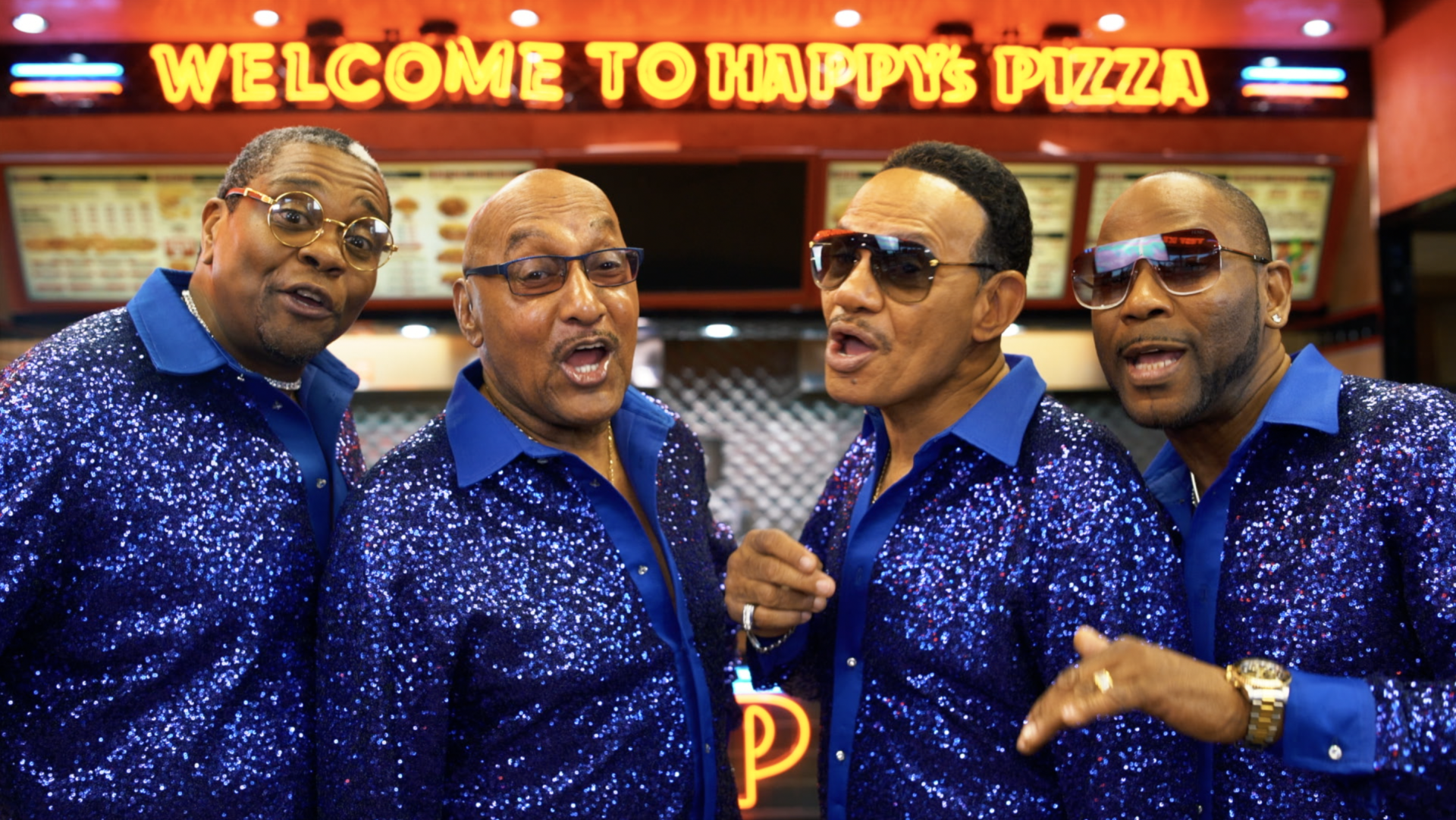 A group of men are standing in front of a sign that says welcome to happy 's pizza