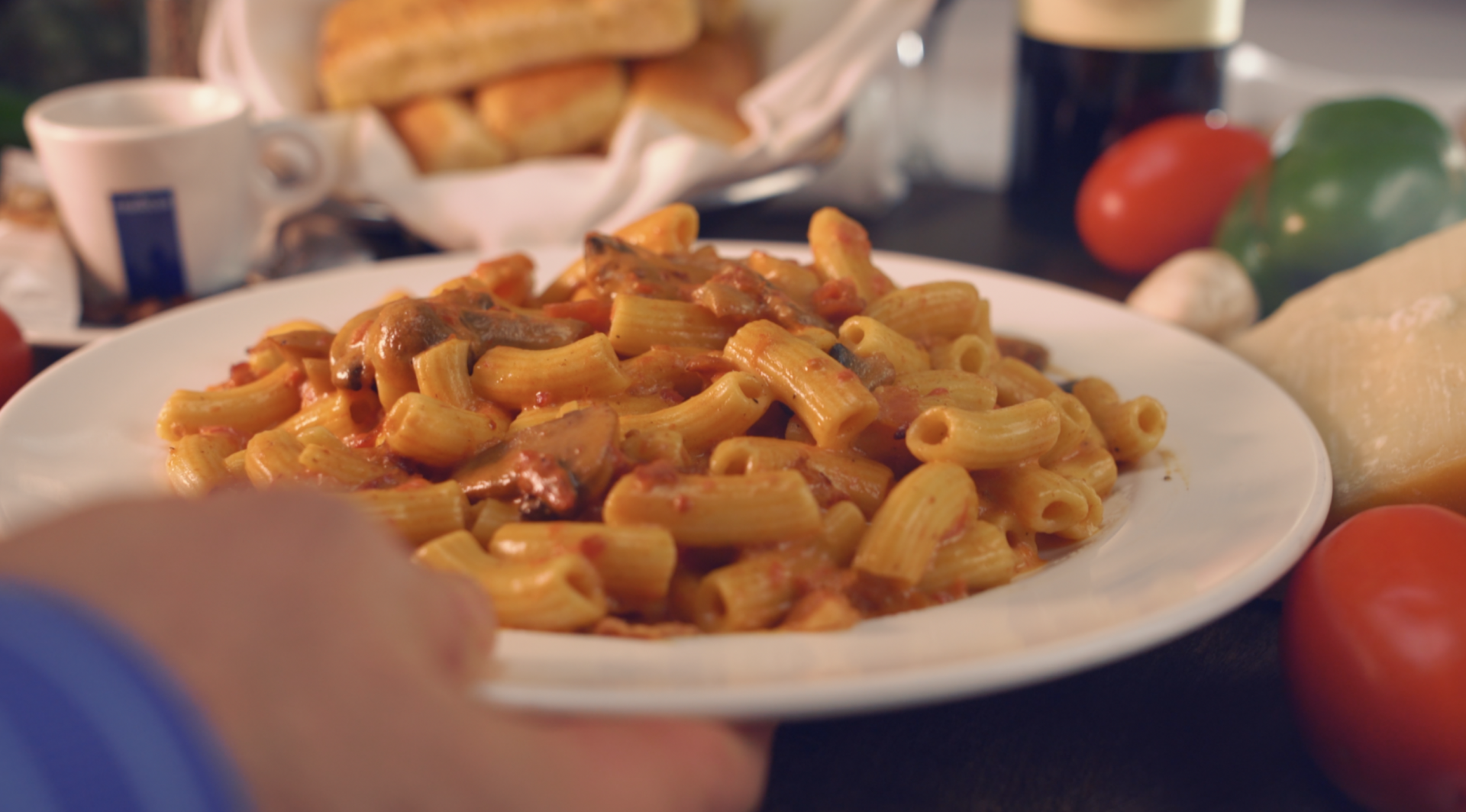 A person is holding a plate of pasta on a table.
