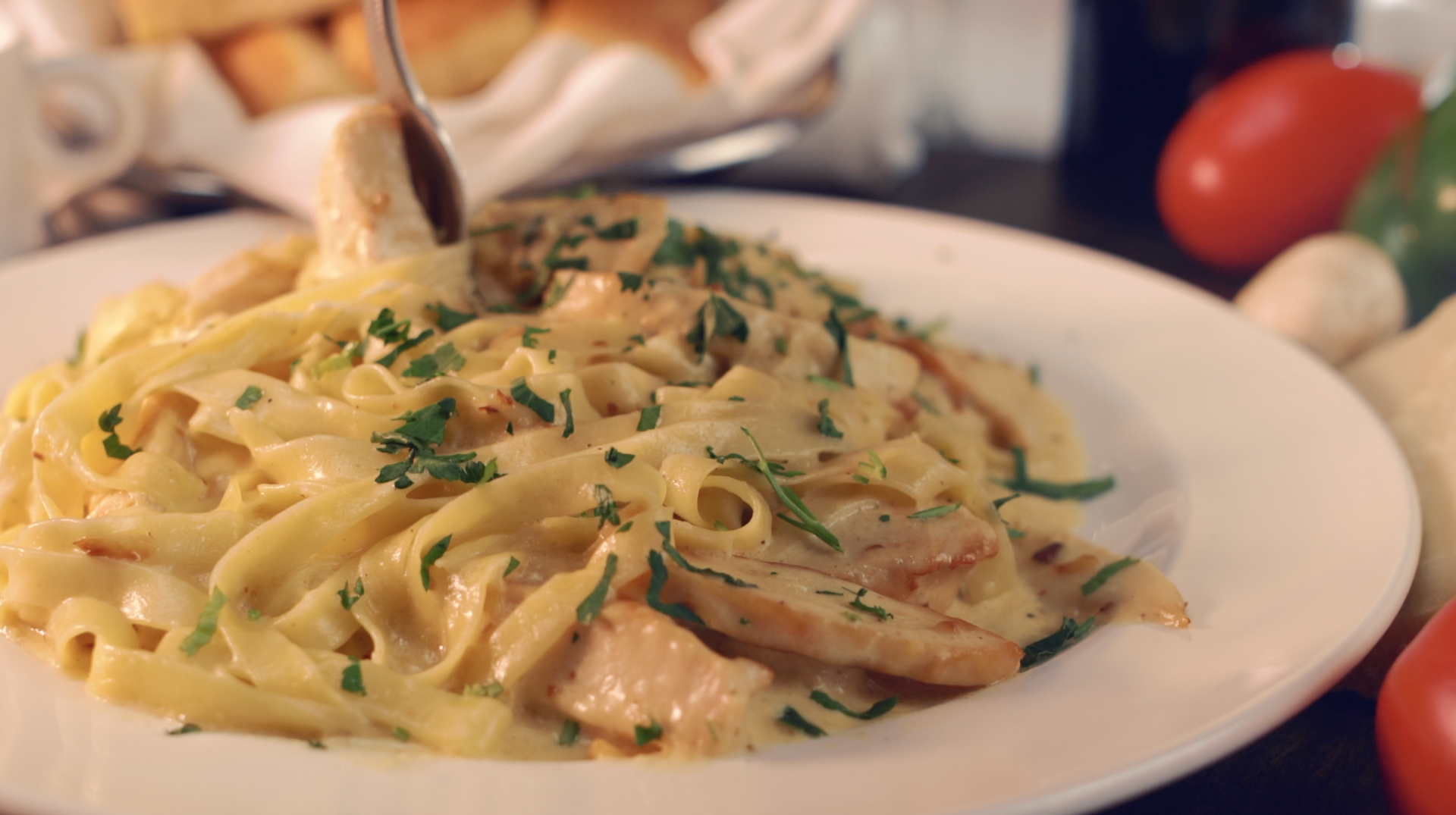 A plate of pasta with chicken and a fork on a table.