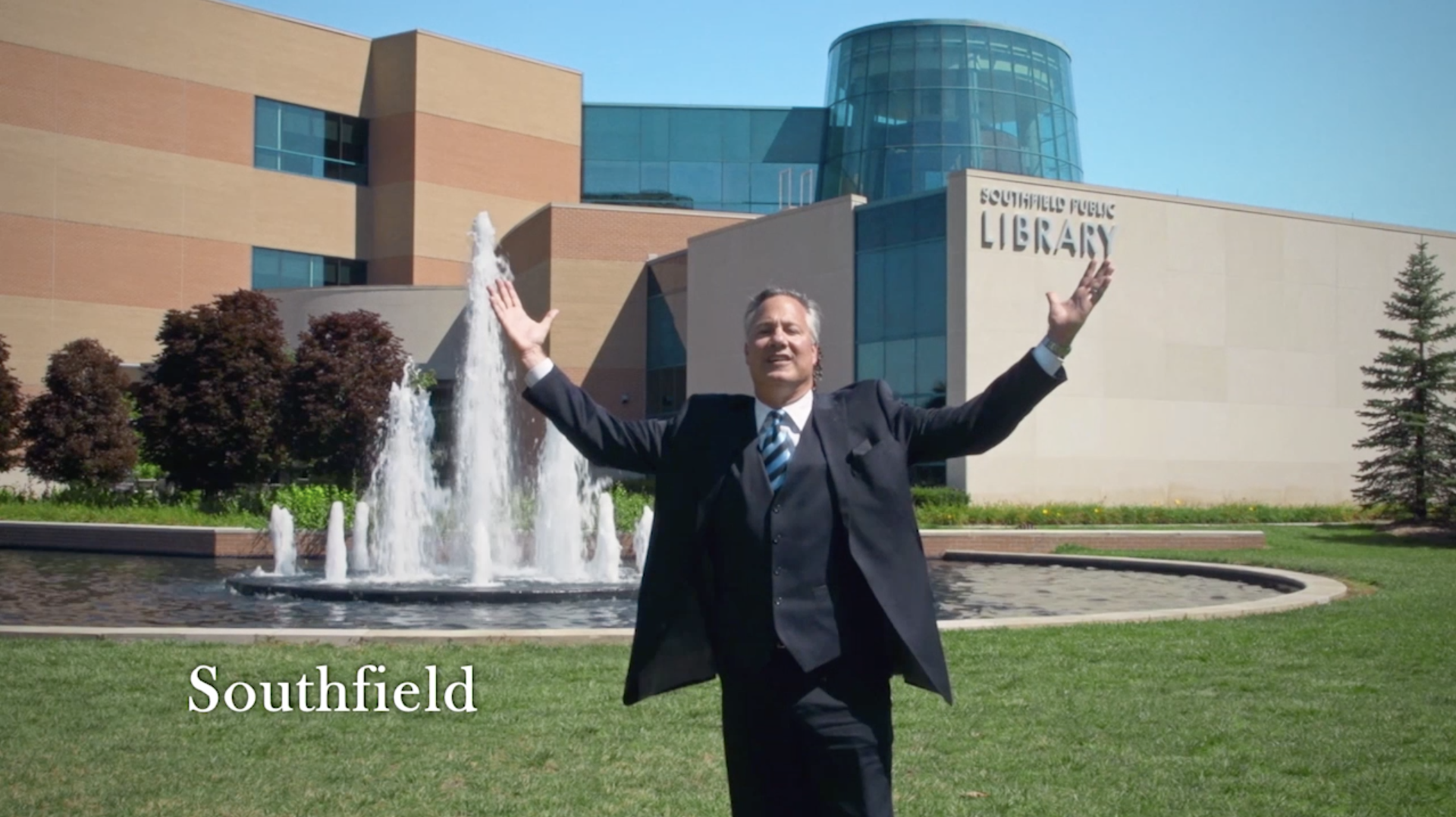 Harry Glans is standing in front of a library with his arms outstretched.