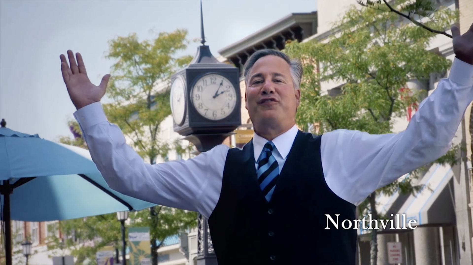 Harry Glans is standing in front of a clock with his arms outstretched.