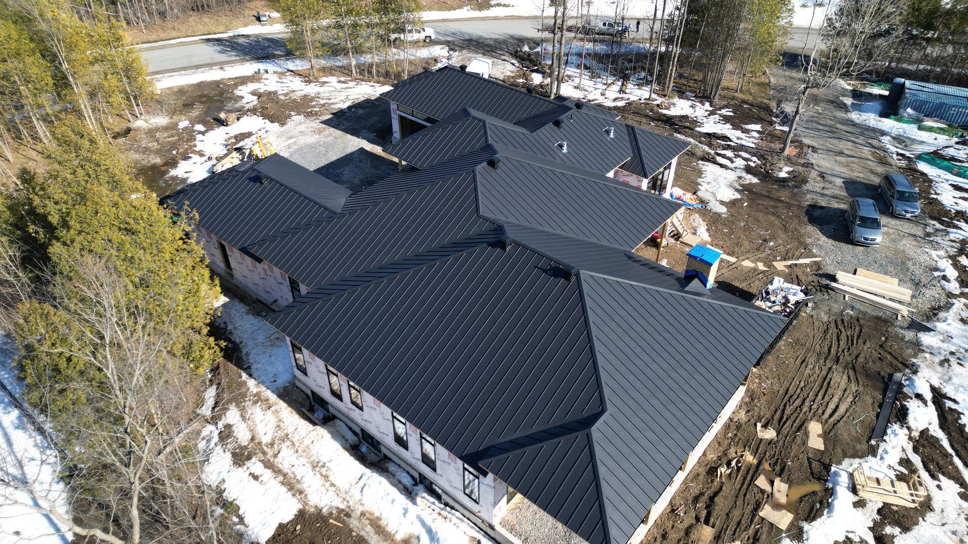 Une vue aérienne d'une grande maison avec un toit noir entouré de neige et d'arbres.