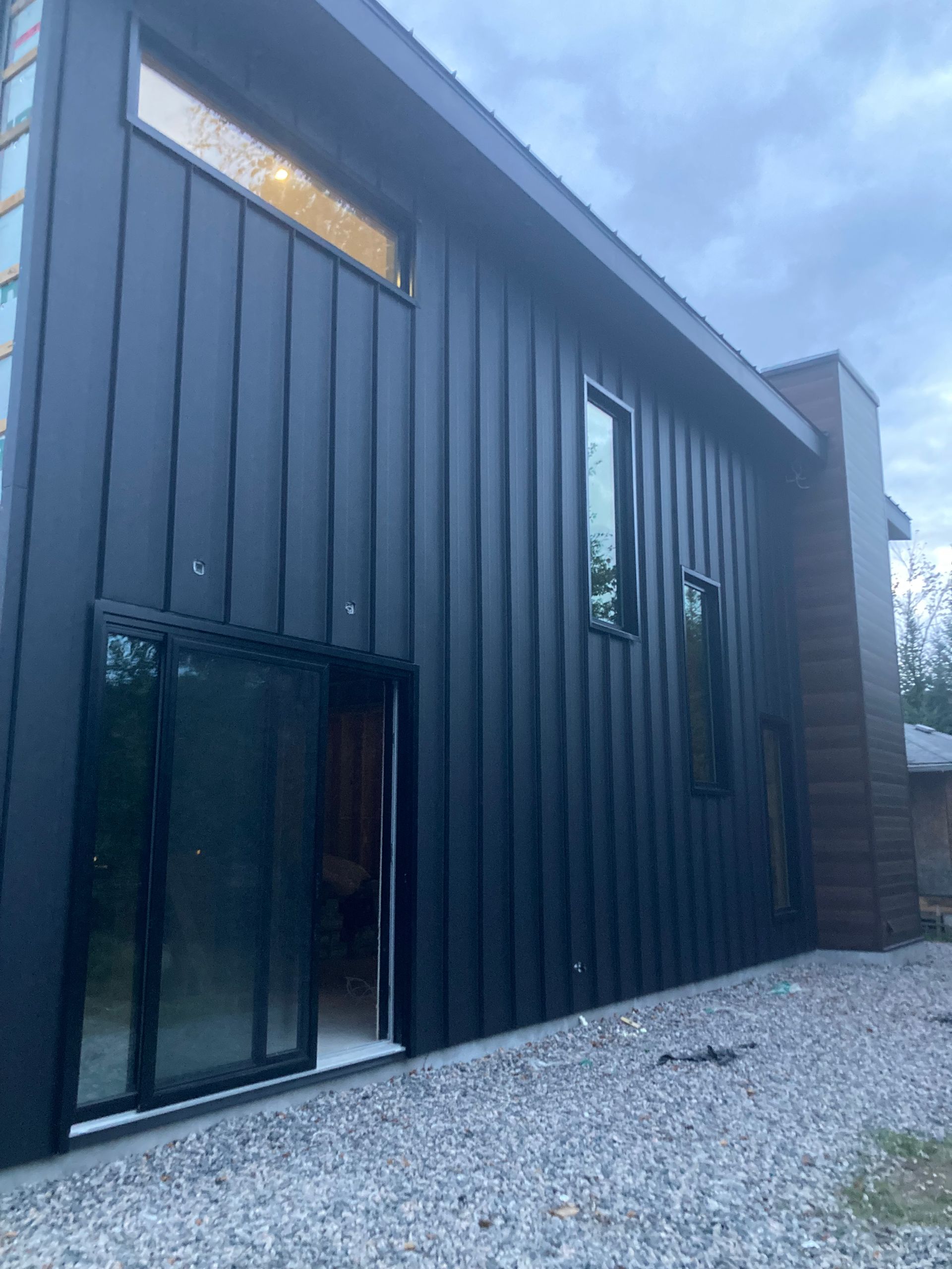 Une maison noire avec beaucoup de fenêtres et une porte coulissante en verre.