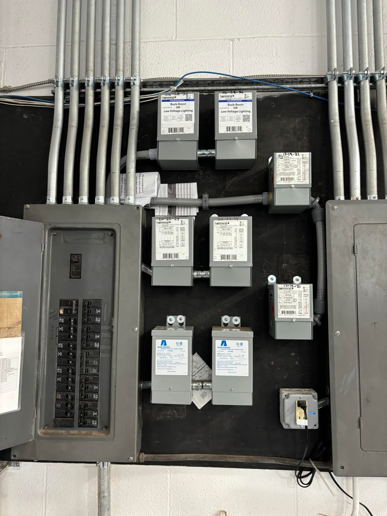 Electrical panel with circuit breakers, meters, and conduit pipes on a wall.