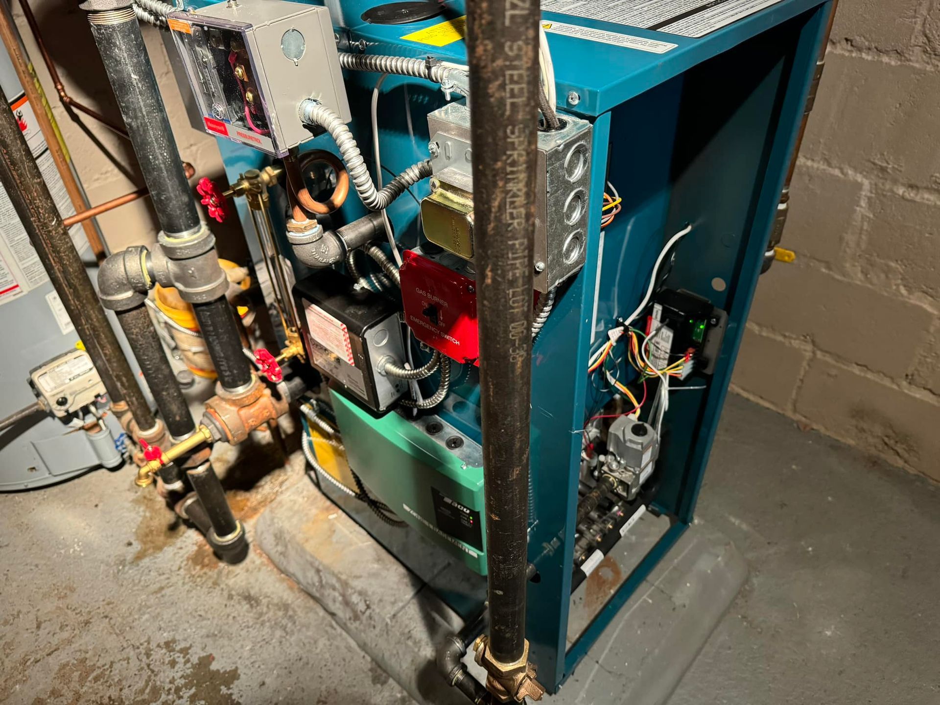 Blue heating boiler with pipes and electrical components in a basement setting.