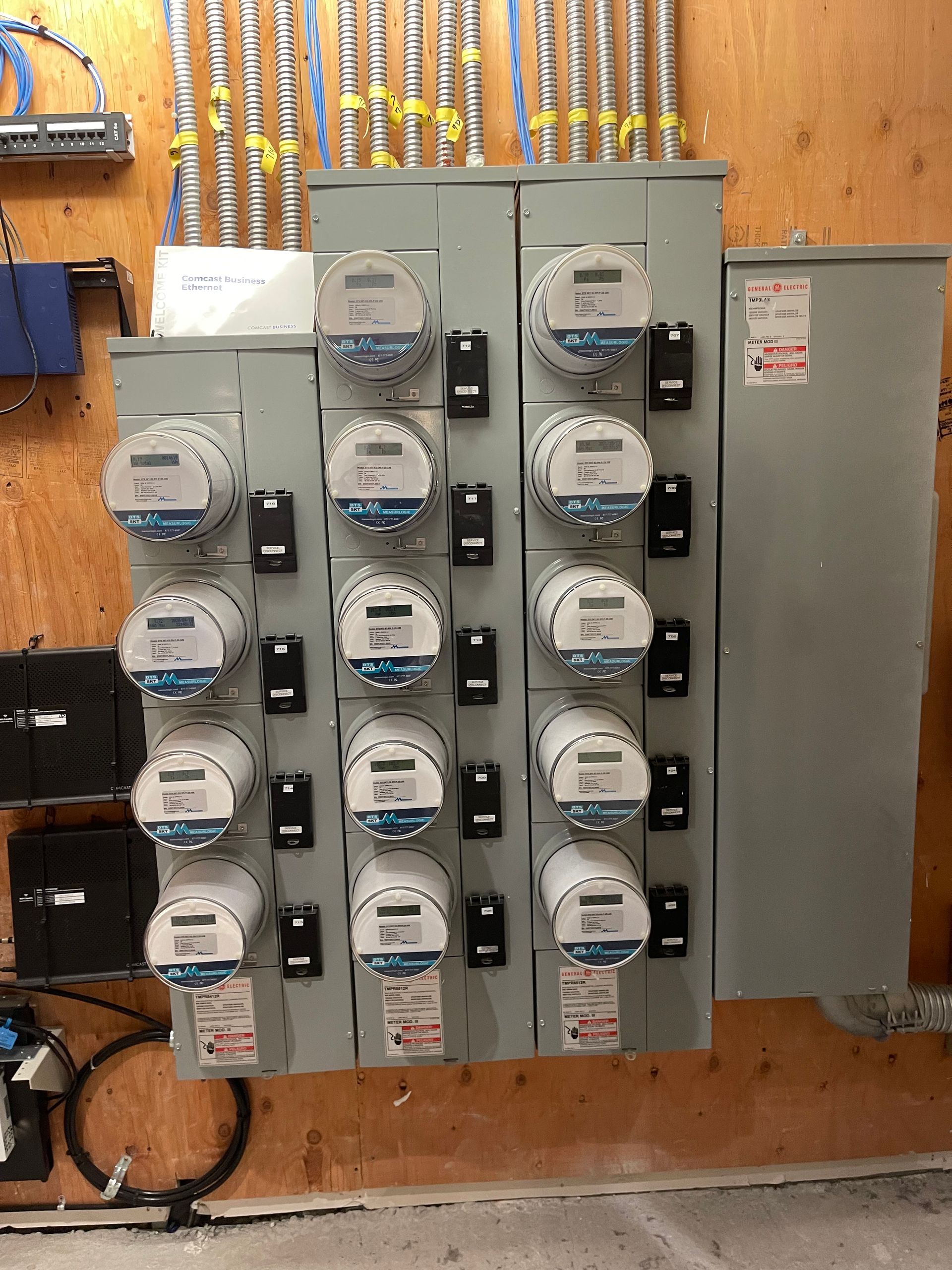 Electric meters on a panel in a commercial setting, with various wires and conduits.