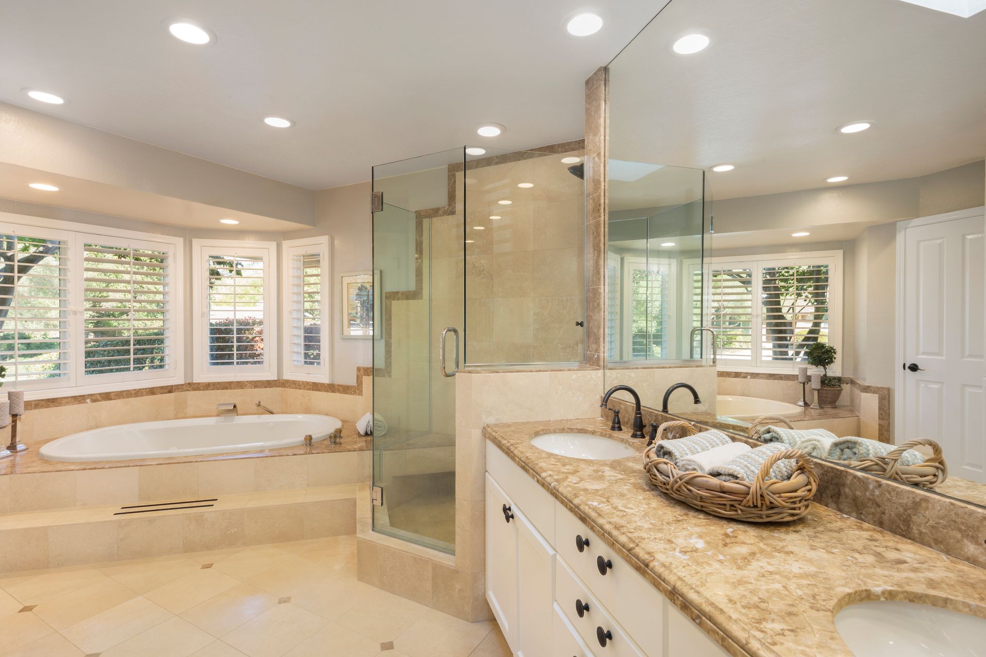 Luxurious beige bathroom with a glass shower, soaking tub, and granite vanity under recessed lights